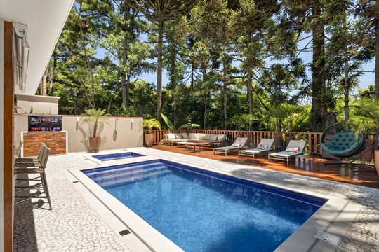 Pileta moderna con deck y sillones en medio de bosque frondoso — proyecto PISCINA DOS SONHOS, por Volpi Arquitetura, en Curitiba