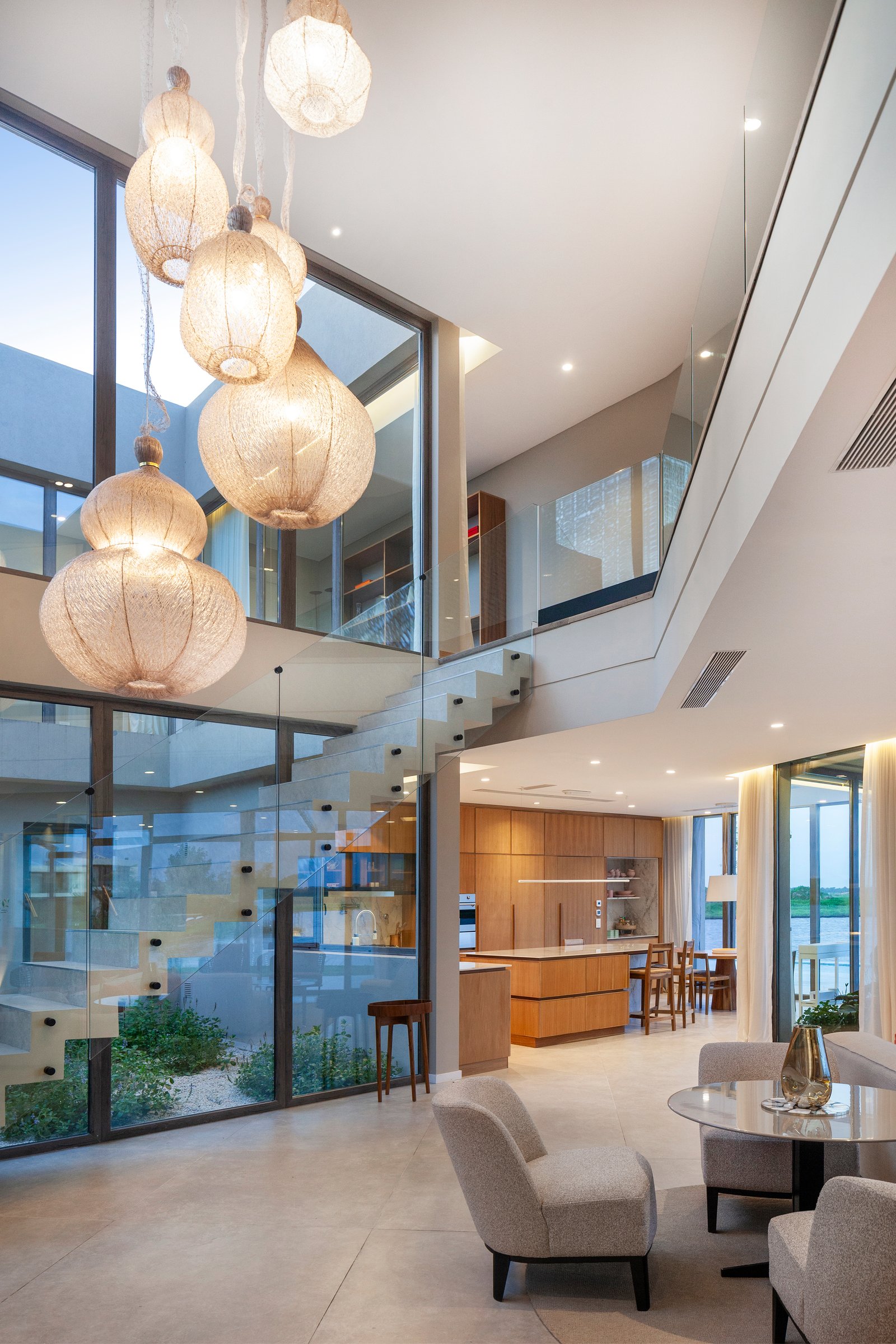 Living moderno con atrium doble altura y luces colgantes — proyecto CASA M40, por A'PRIMA - Arquitectura Sustentable, en Unnamed Road
