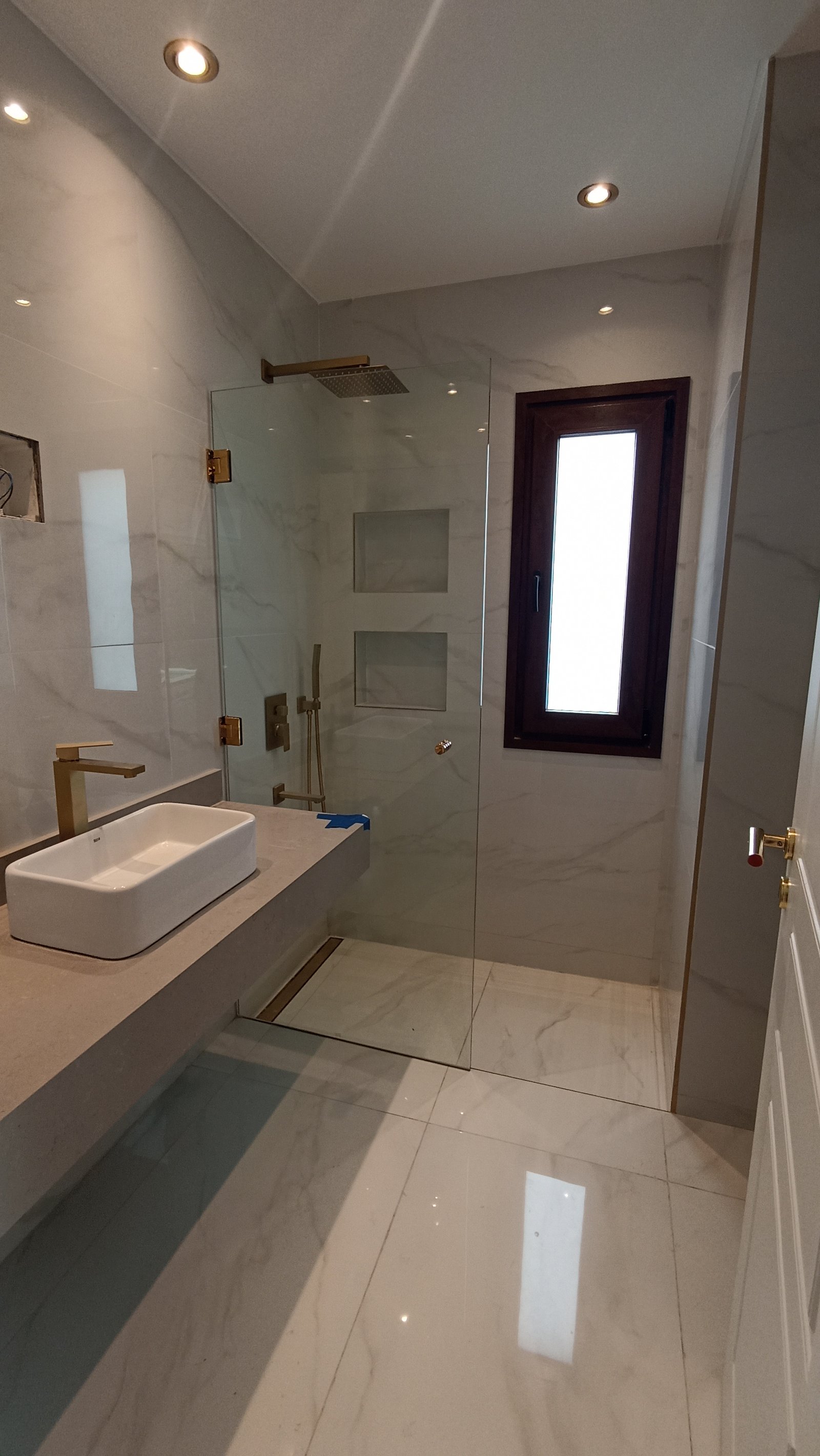 Baño moderno con mármol, ducha de cristal y grifería dorada — proyecto Vivienda en Fincas de Hudson, por Monarq Arquitectura, en C. 137 7400