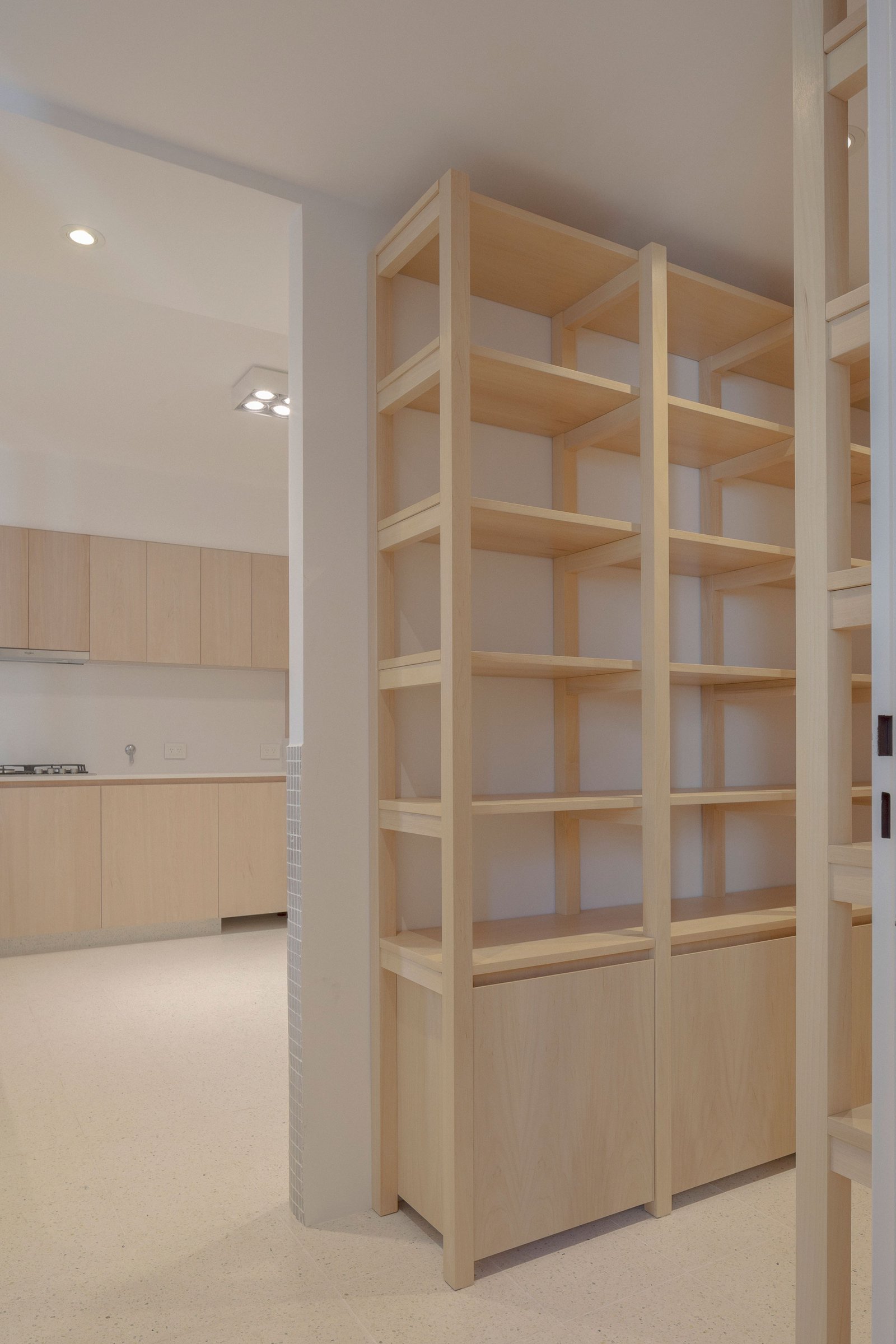 Cocina minimalista moderna con estanterías de madera clara y luz cálida — proyecto Reforma O'Higgins, por Estudio YME, en Belgrano