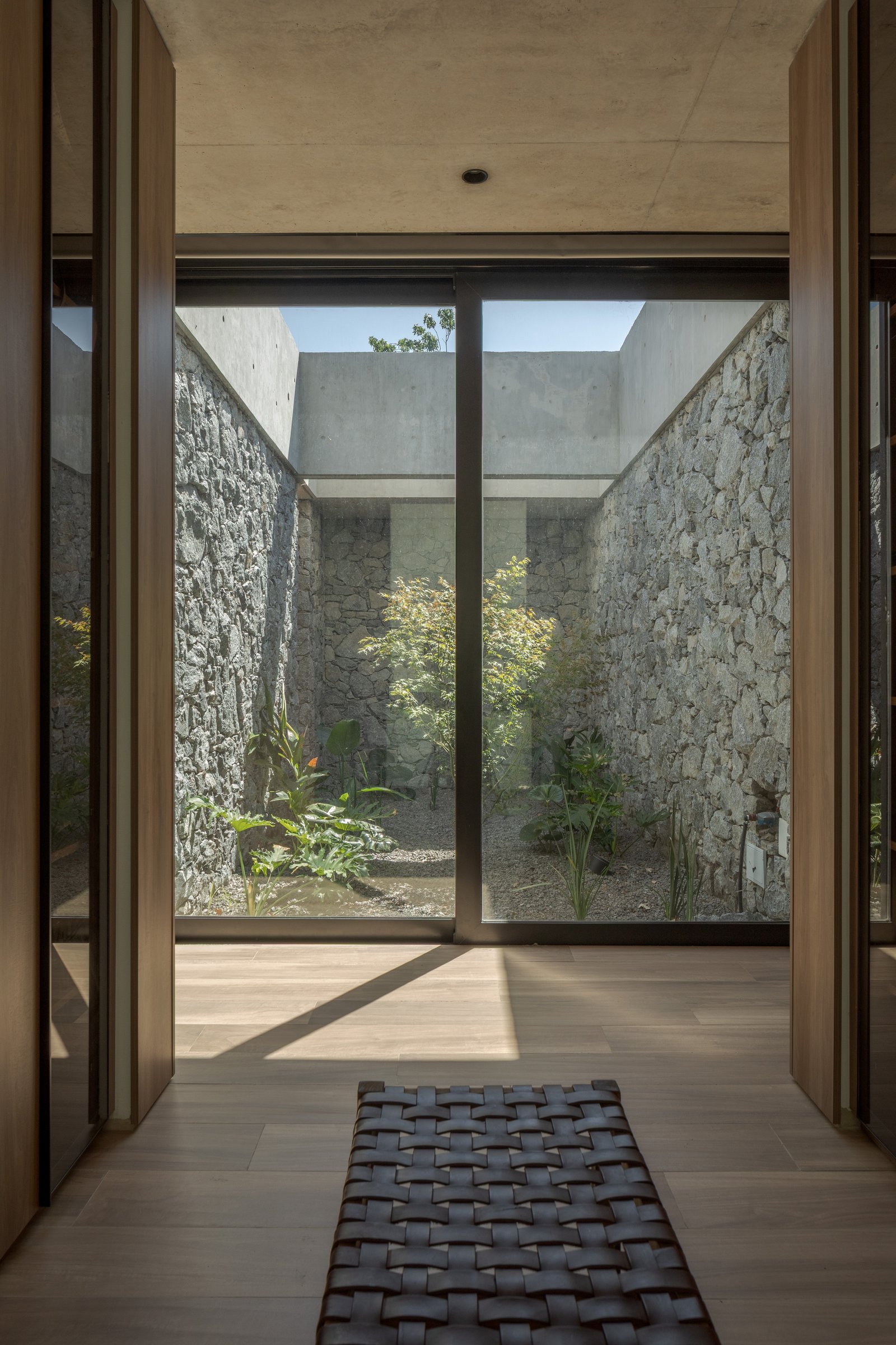 Patio moderno con muros de piedra y grandes ventanales — proyecto Casa PLANALTO, por Grupo CRBN, en Av. Pres. Perón 10298