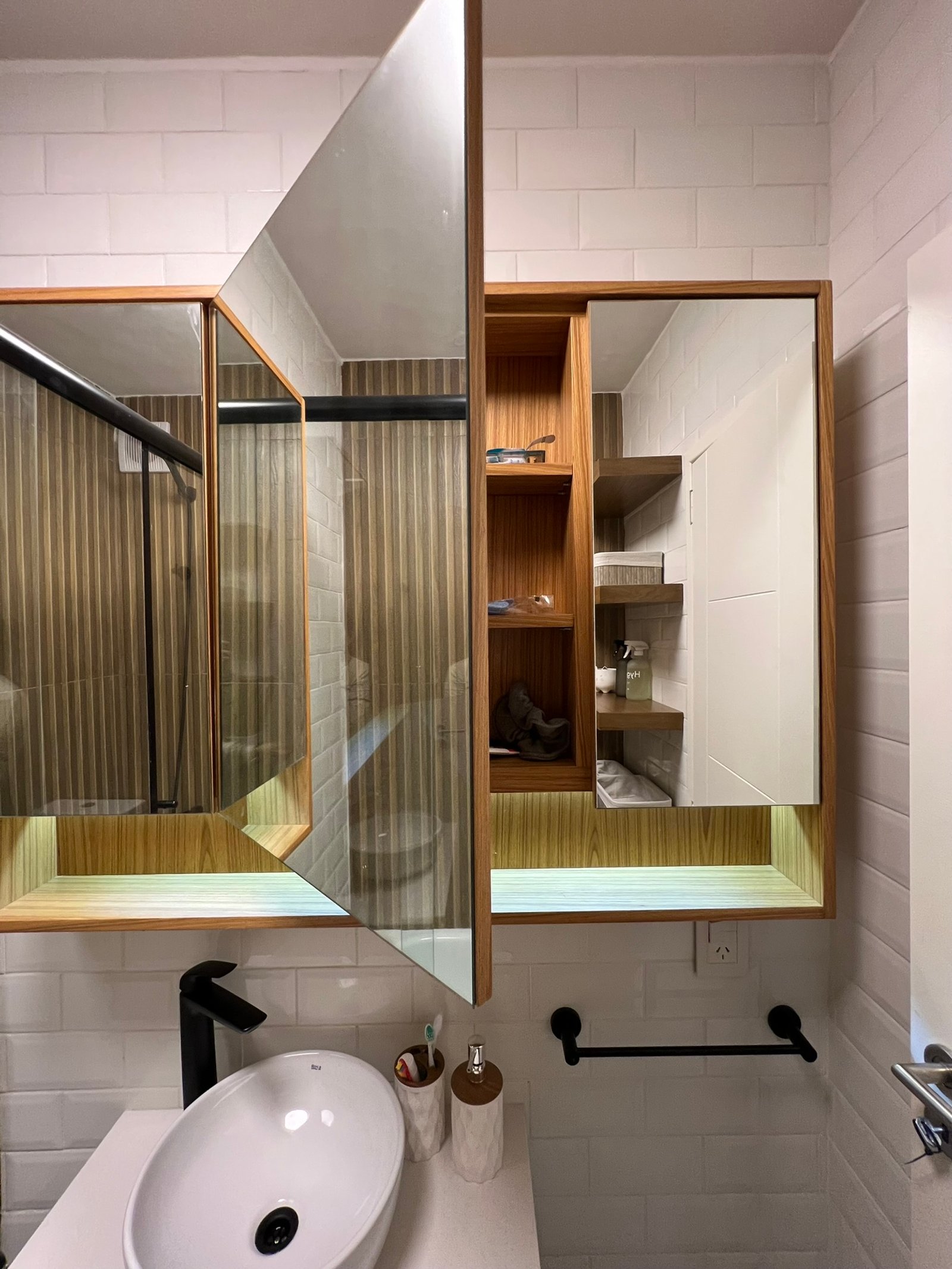 Baño moderno con espejo geométrico, lavabo ovalado y detalles en madera — proyecto Perón , por MDBK Arquitectura, en Barrio Norte