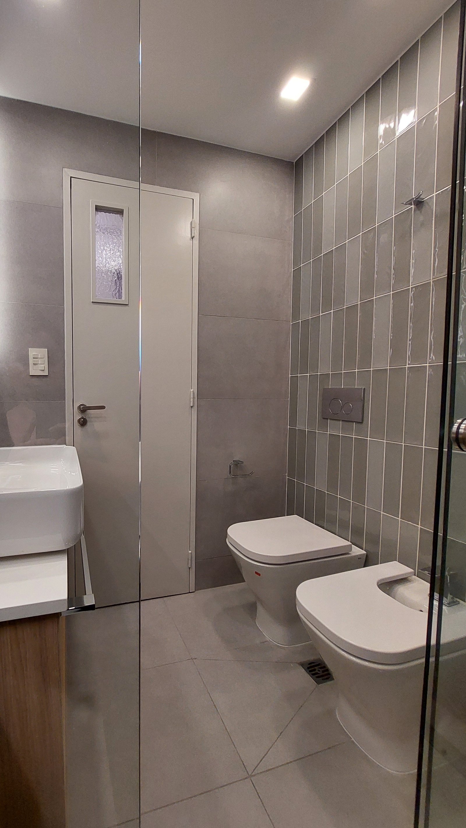 Baño moderno con azulejos grises y dos inodoros — proyecto FLORES, por Arquitecta, en Flores
