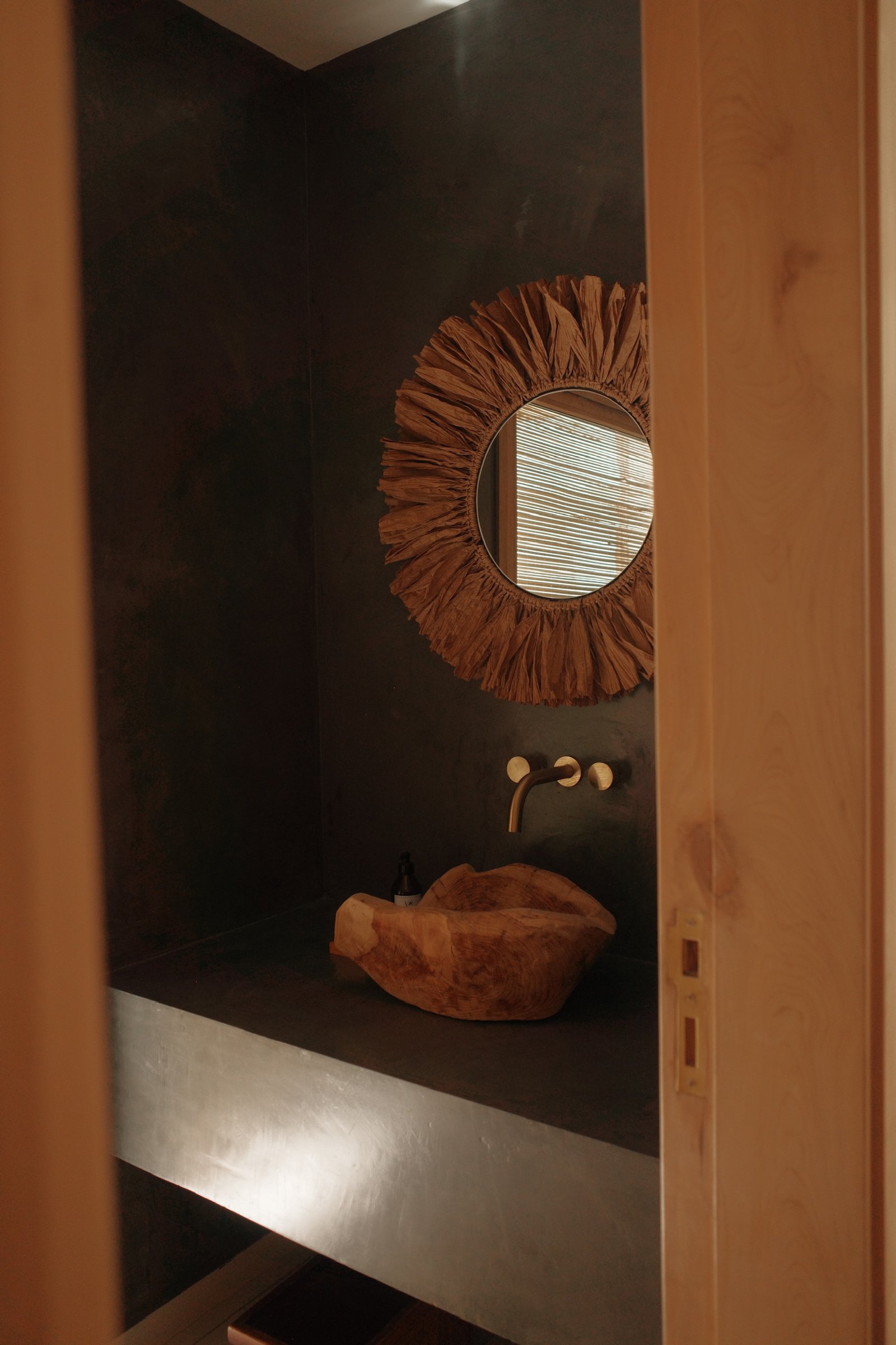 Baño rústico con bacha de madera, espejo de ratán y paredes texturizadas — proyecto Casa Refugio, por Jeitinho Estudió Creativo, en Neuquén