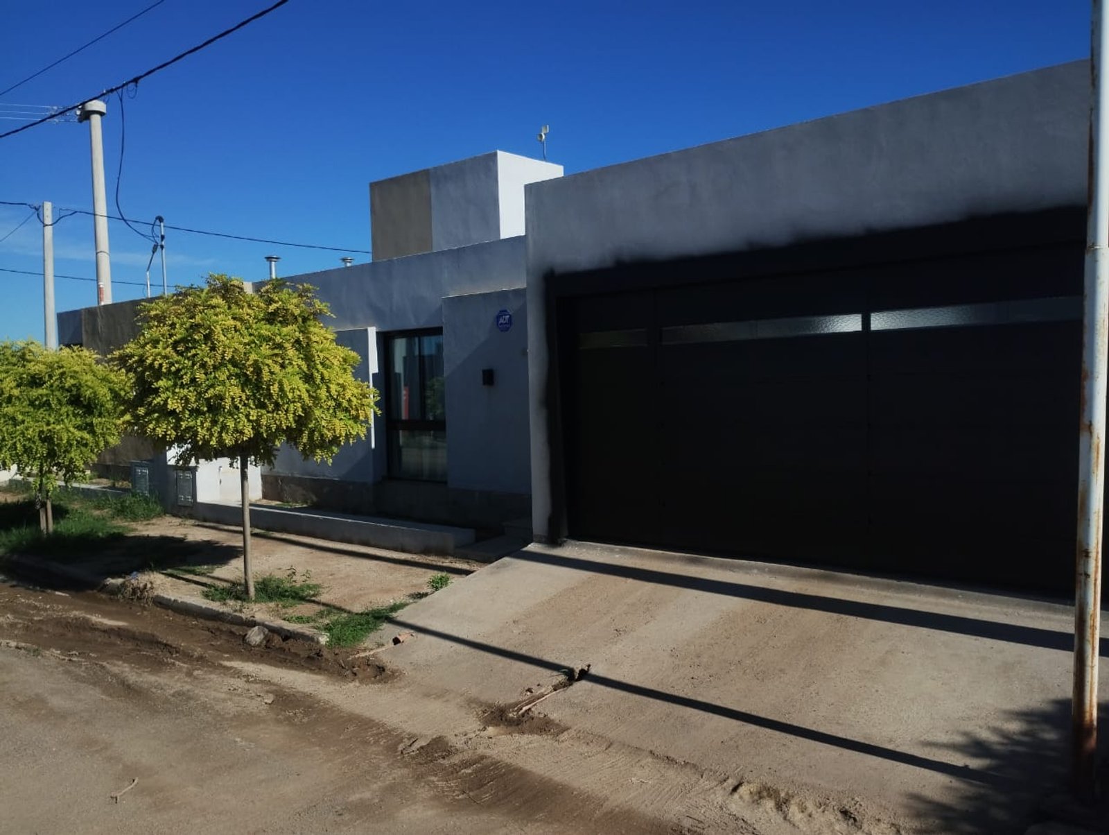 Fachada de casa moderna suburbana con puerta de garaje oscura y árbol frondoso — proyecto FACHADA S&S, por Todo con A, en X5125 Monte Cristo