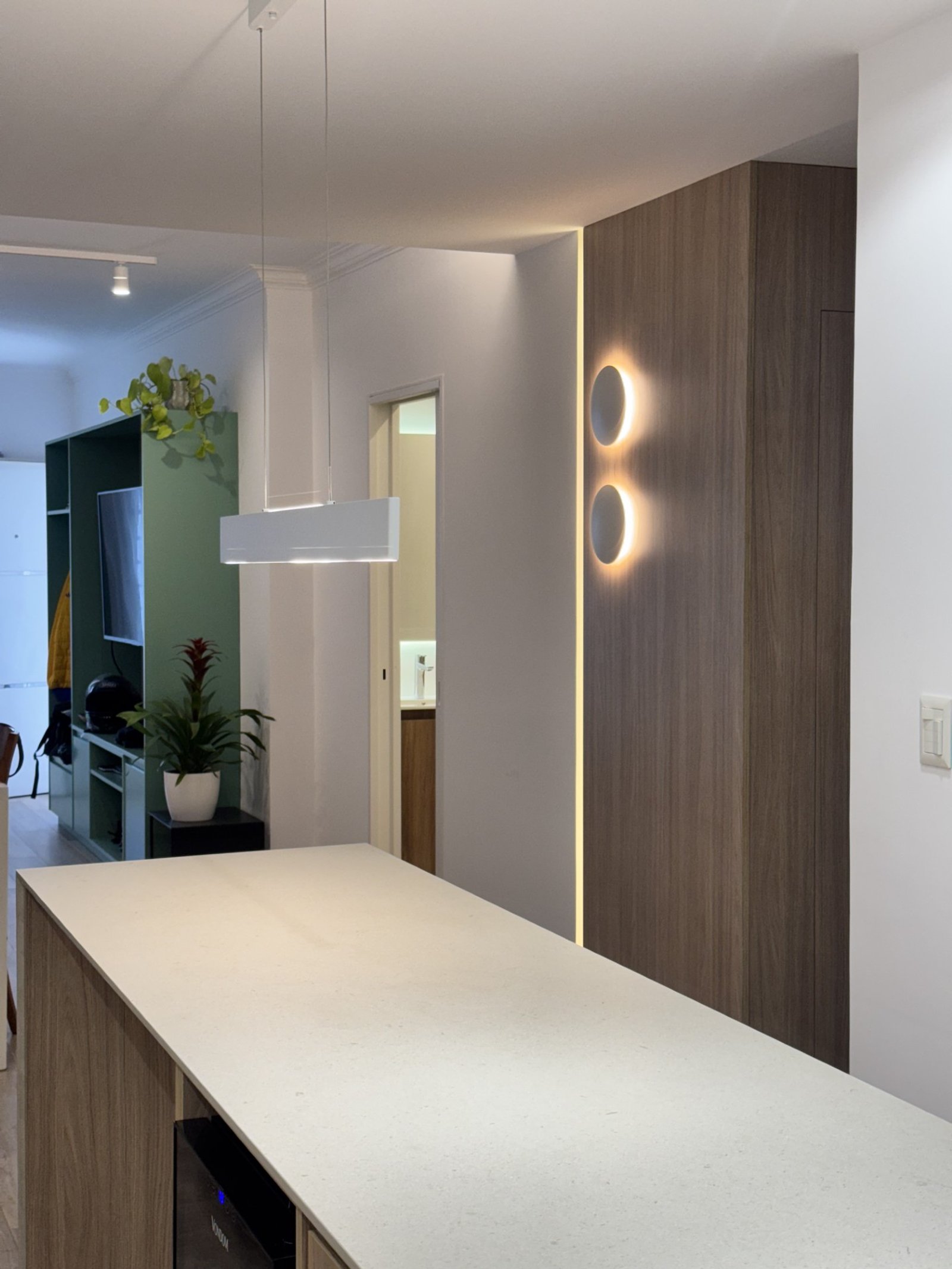 Cozinha moderna com ilha, iluminação indireta e painéis de madeira escura — projeto CASA LEAN, por Estudio Grupo 32, em Vicente López