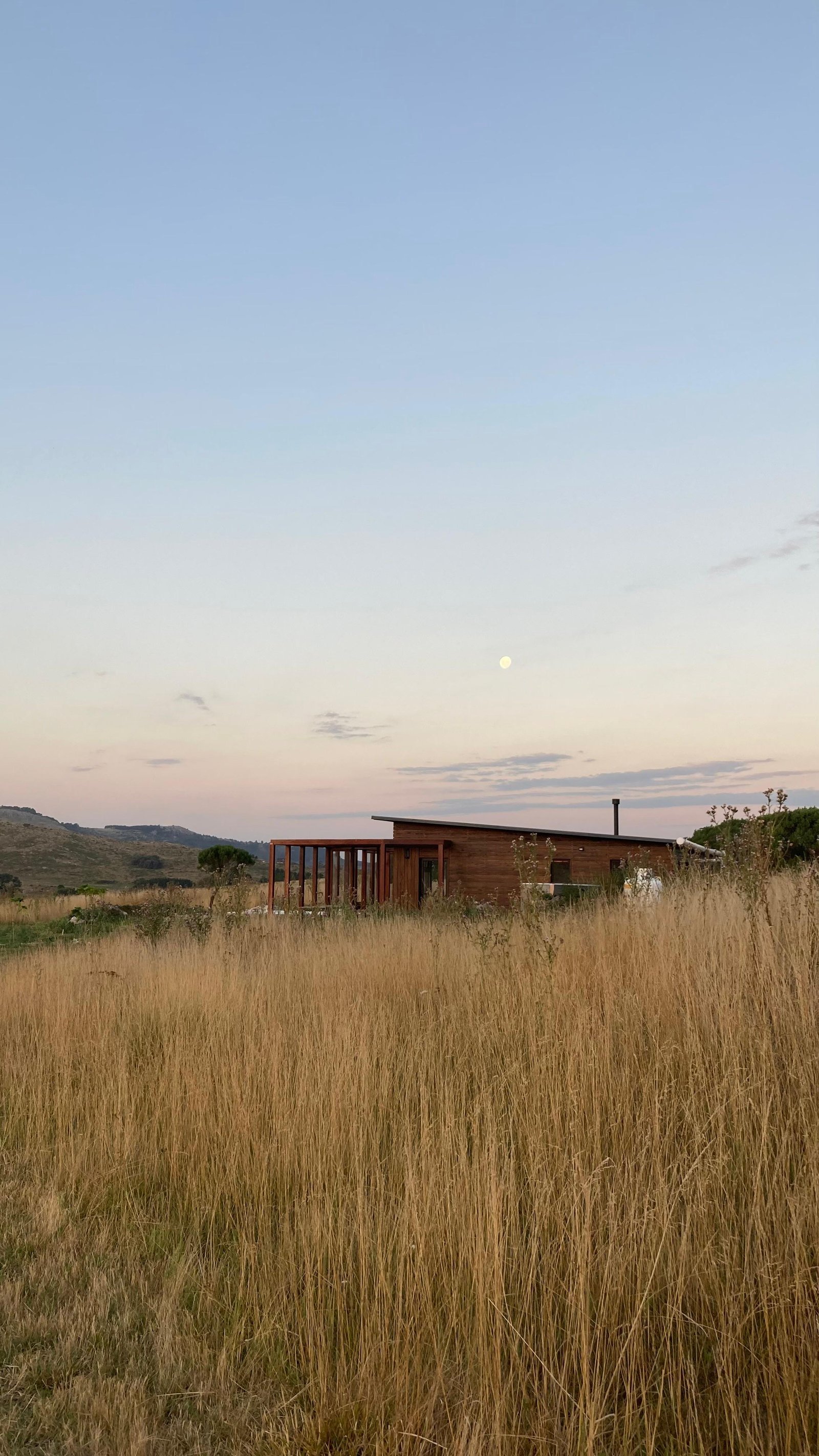cabaña moderna de madera en campo seco con luna llena — proyecto El Reparo, por Wompa, en Tandil