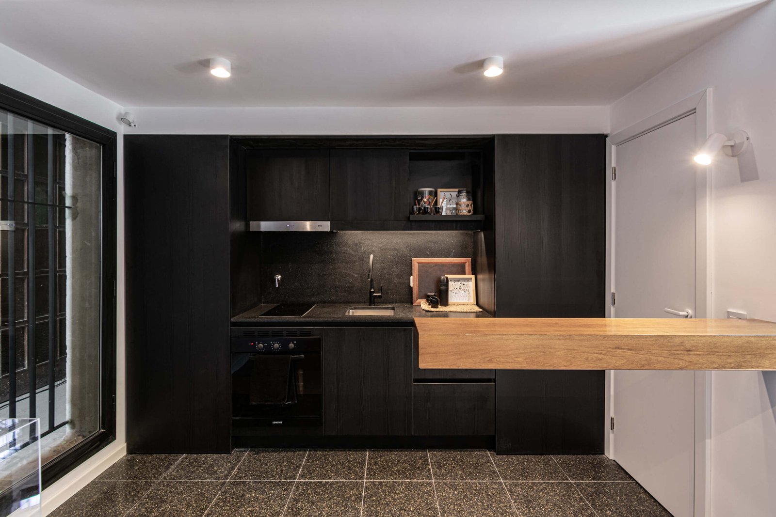Cocina moderna negra con mesada de madera y piso de piedra — proyecto Showroom EDIFICIO PATRIMONIO, por DIB OBRIST Arquitectas, en Rosario