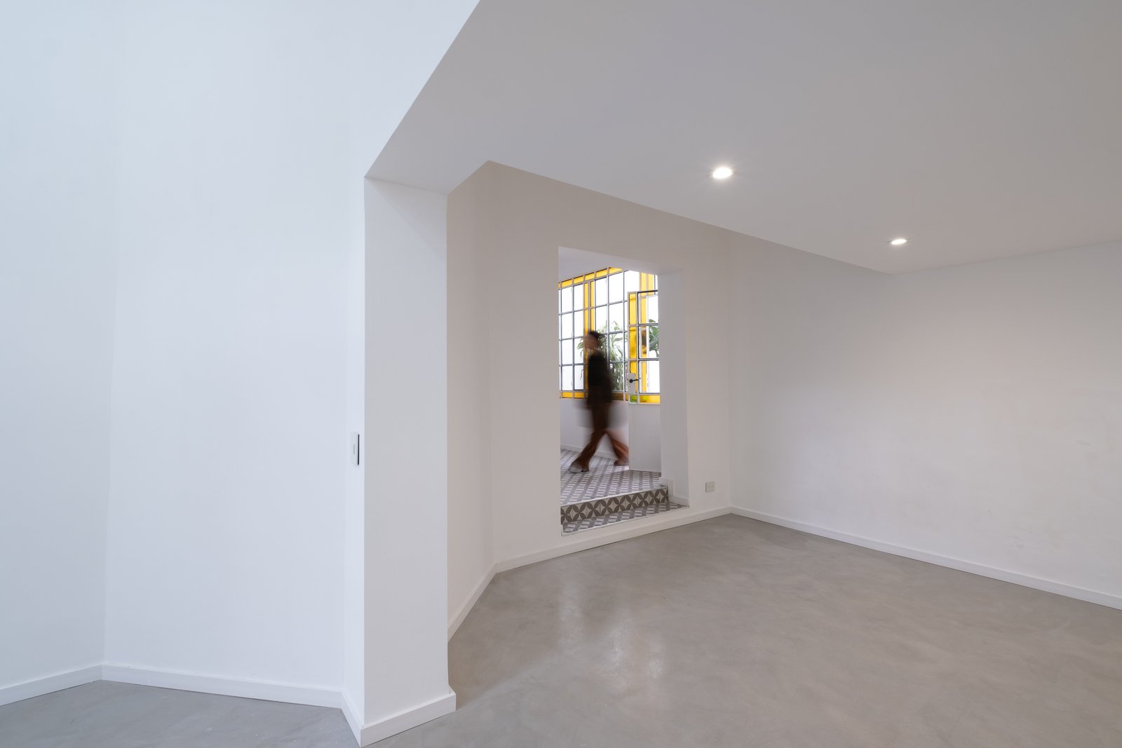 espaço moderno com janela circular amarela e piso de cimento — projeto Casa Patio, por Herrera Ungaro, em San Cristóbal
