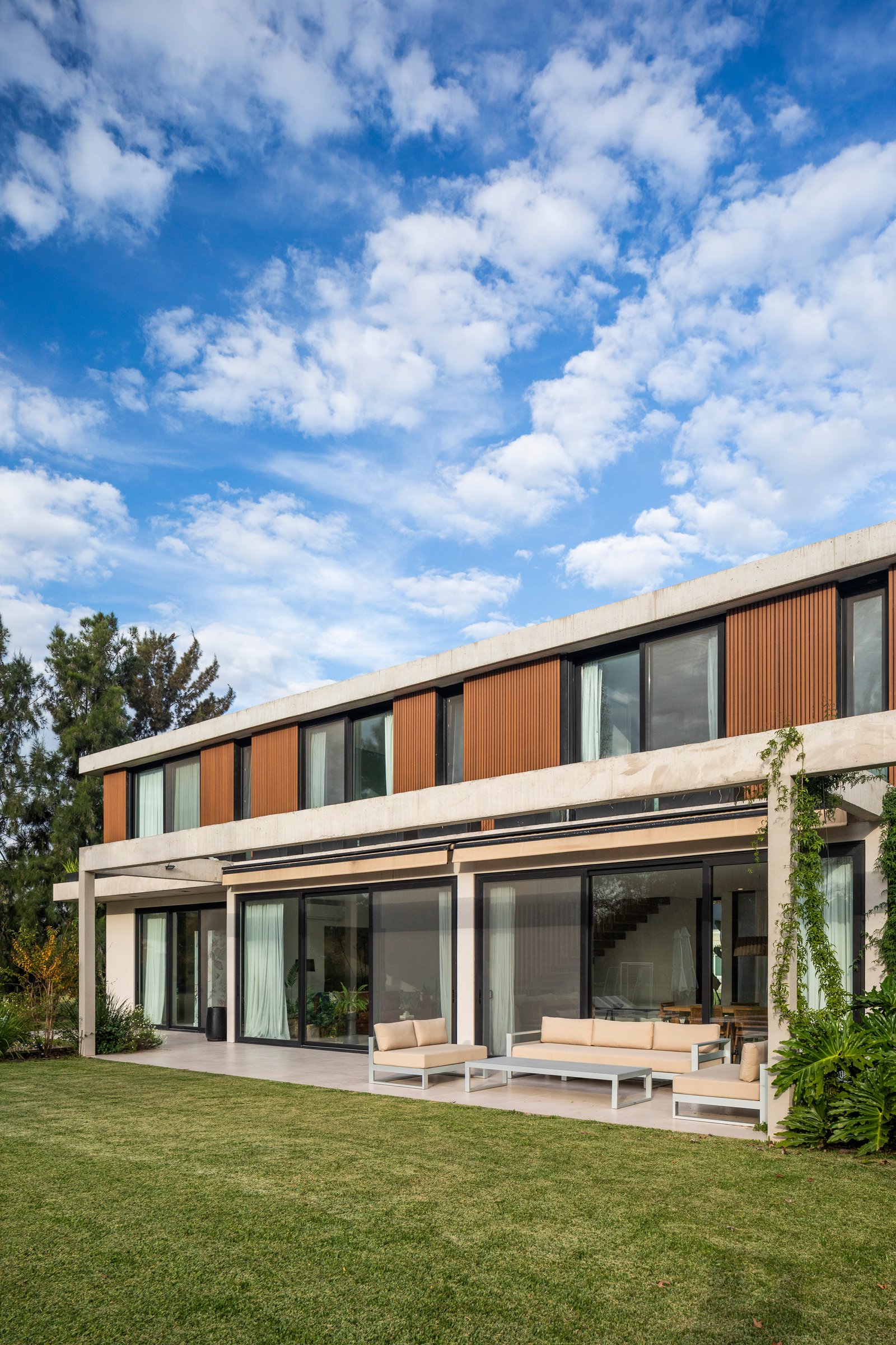 Fachada moderna con revestimiento de madera y amplios ventanales — proyecto CASA HS143, por A'PRIMA - Arquitectura Sustentable, en km 7.5 Ruta 25