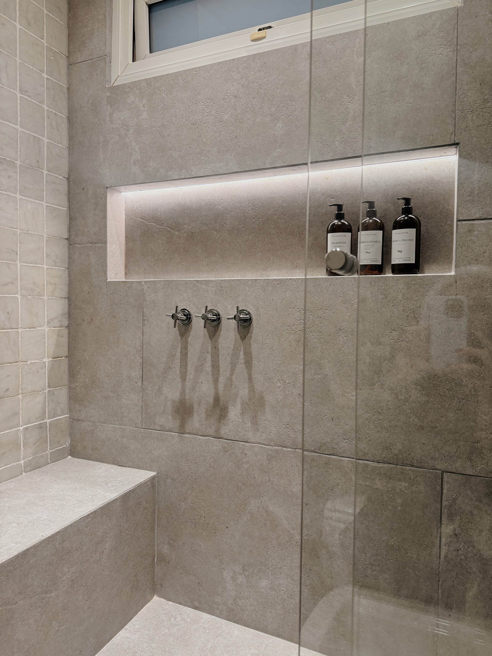 Baño moderno con nicho iluminado, grifería y bancos de piedra — proyecto Virrey Loreto, por Estudio BDM, en Buenos Aires