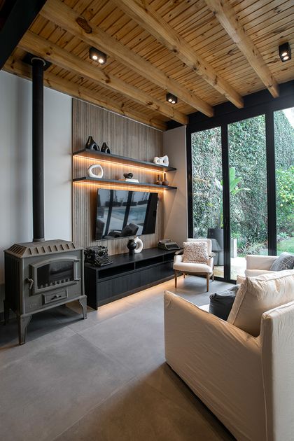 Living moderno con techo madera, estufa negra y vistas jardín — proyecto Casa Oroño, por Estudio Plats, en Buenos Aires