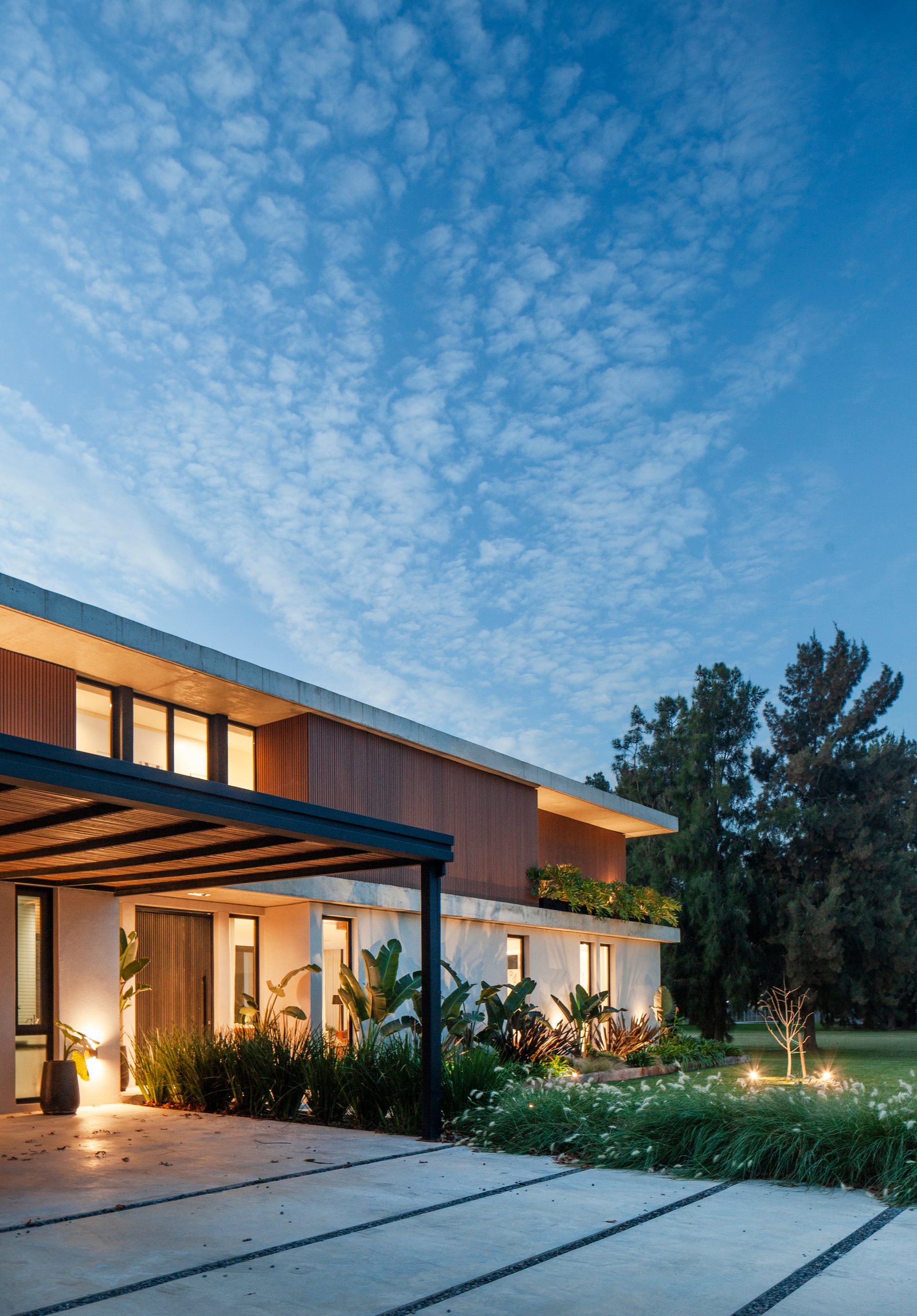 fachada moderna com vegetação e pérgola iluminada — projeto CASA HS143, por A'PRIMA - Arquitectura Sustentable, em km 7.5 Ruta 25