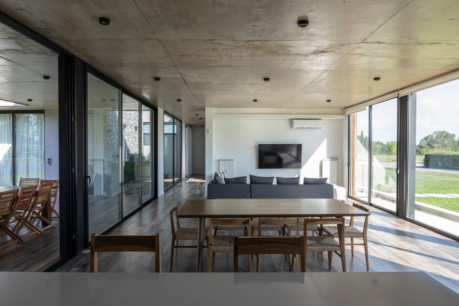 Living comedor moderno con techo de hormigón expuesto y grandes ventanales — proyecto Casa Cruz , por Grupo CRBN, en B2812 Exaltación de la Cruz
