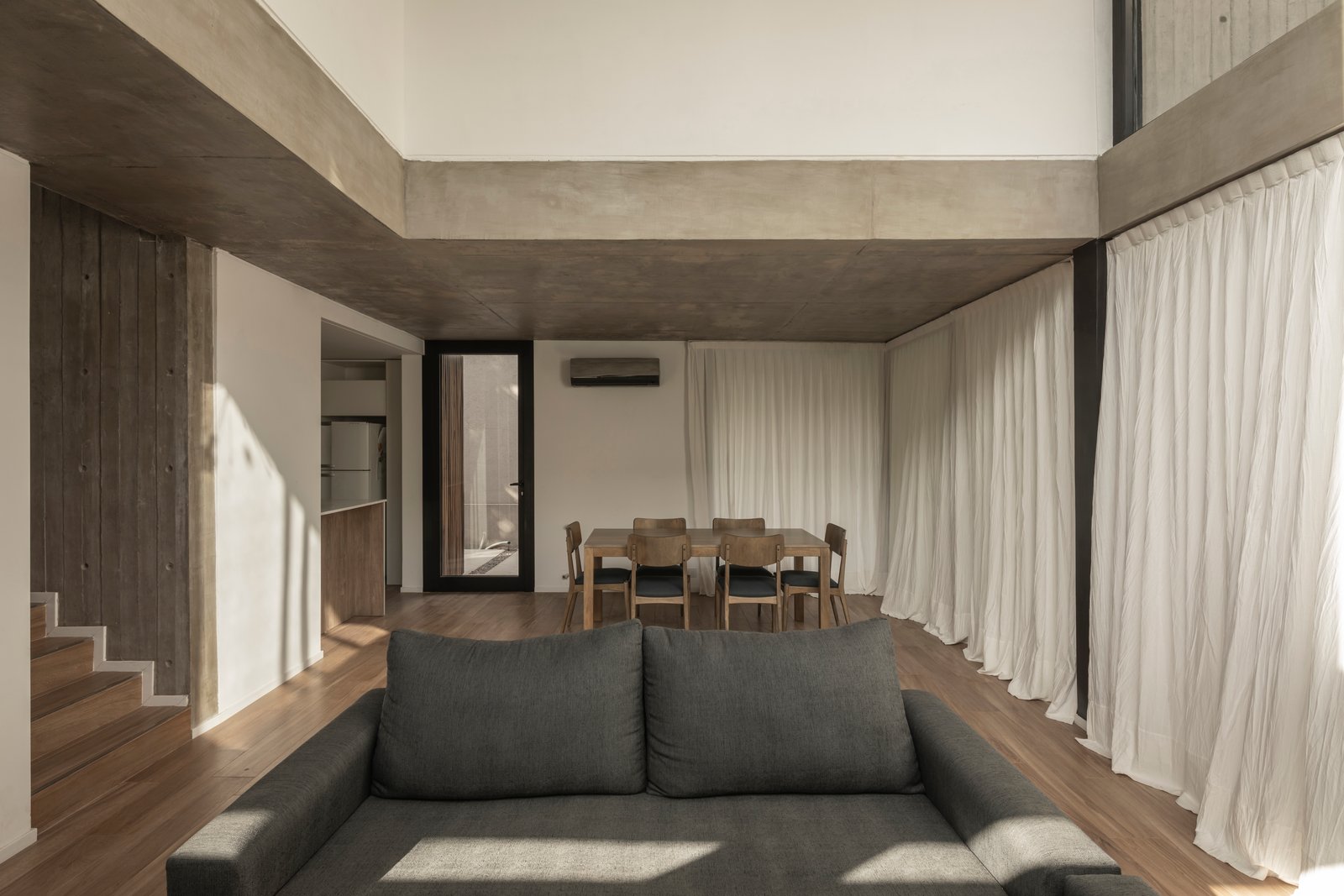 Sala de estar e jantar moderna com concreto aparente e cortinas brancas — projeto Casa Emilia, por Grupo CRBN, em Parque Leloir