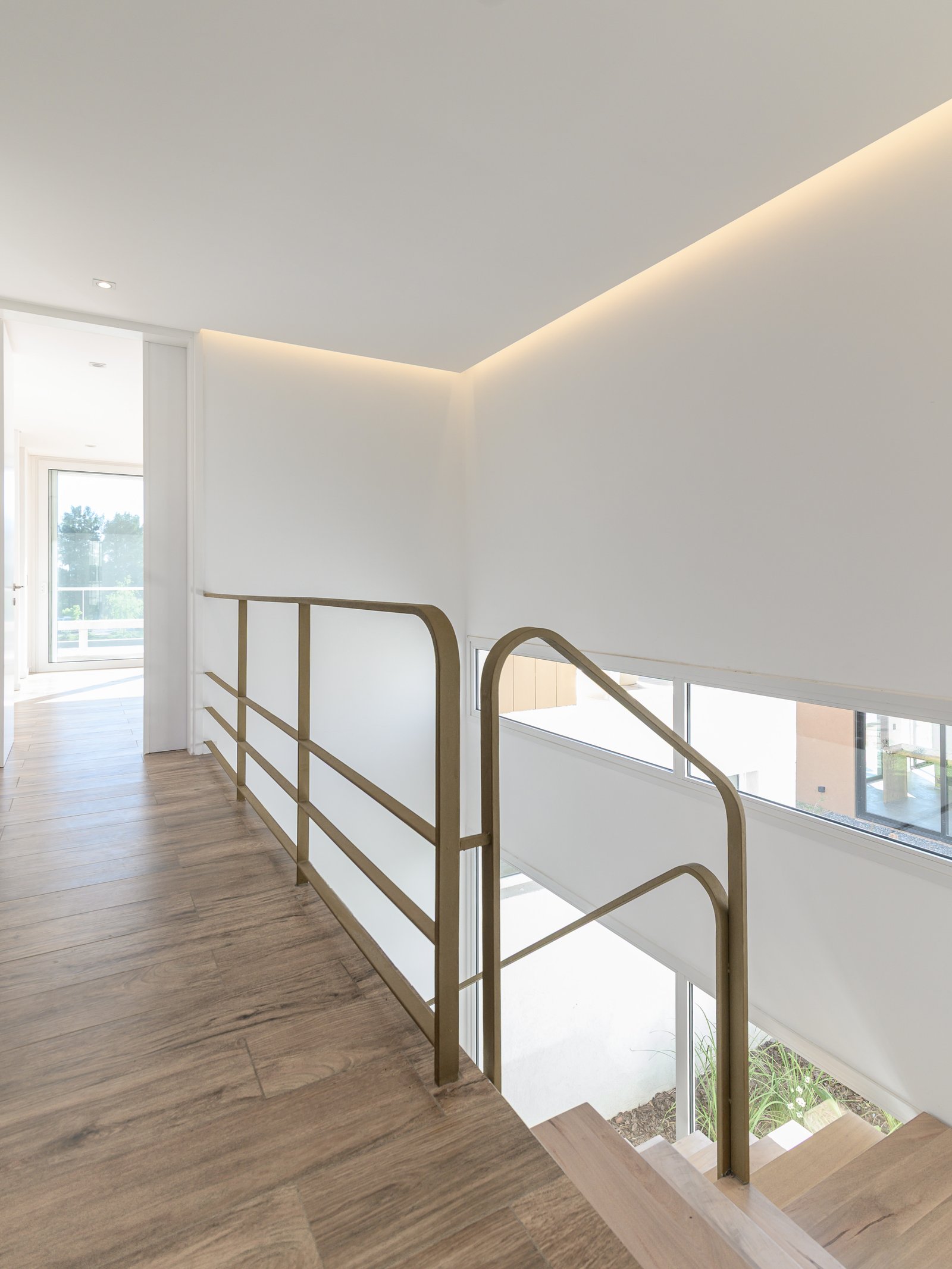 Pasillo y escalera moderna con luz indirecta y baranda de bronce — proyecto CASA CALA, por Auge desarrollos & crowdfunding, en Nordelta