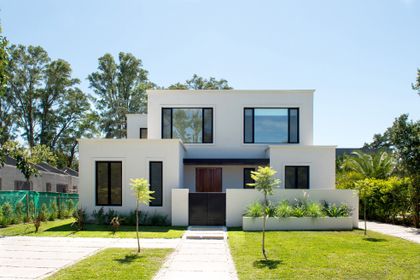 Moderna fachada blanca de casa de dos pisos con grandes ventanas negras — proyecto Bosque Chico, por Estudio Arq. María Sioli, en Garin