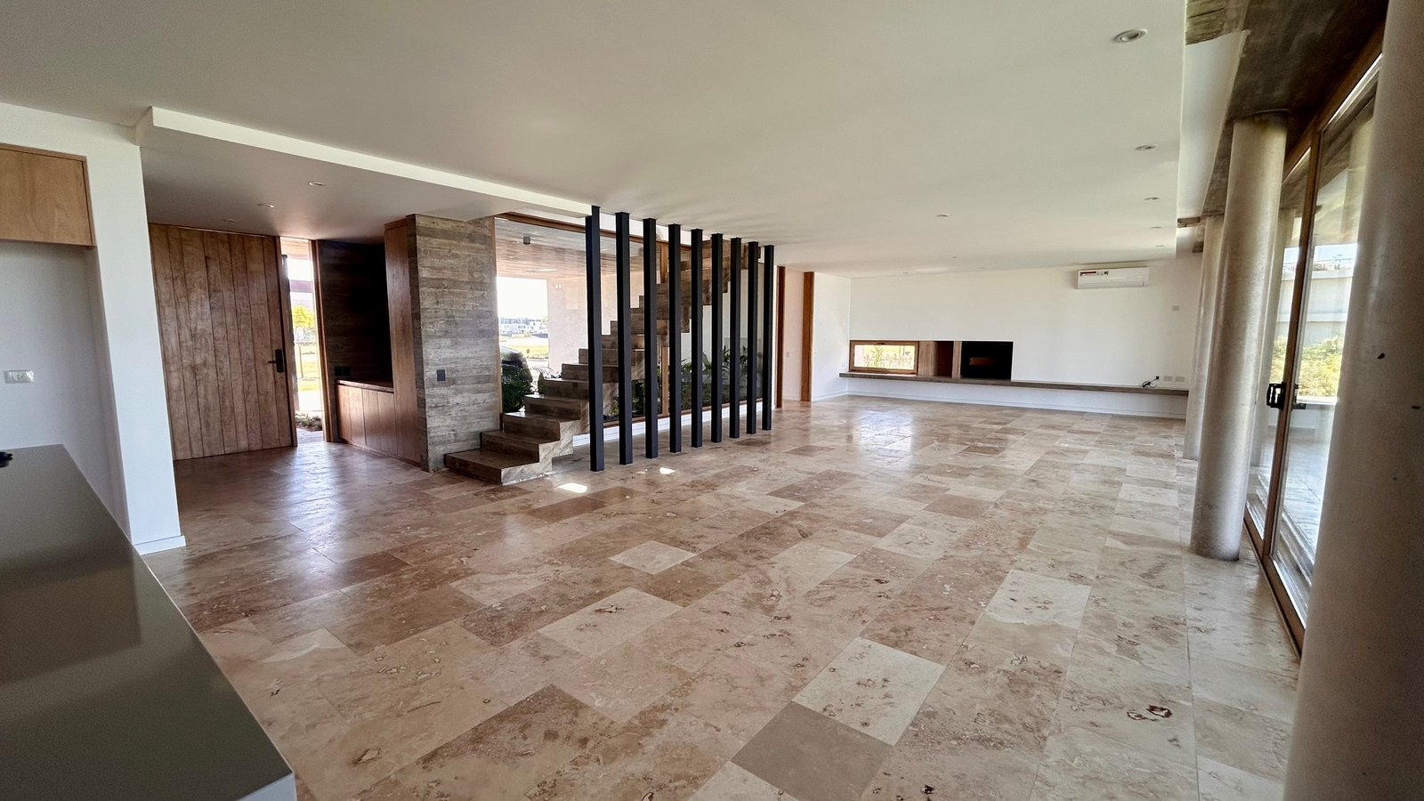 Living moderno con suelo de travertino y escalera flotante — proyecto Casa Puentes, por Guerrero Arquitectos, en Rincón de Milberg