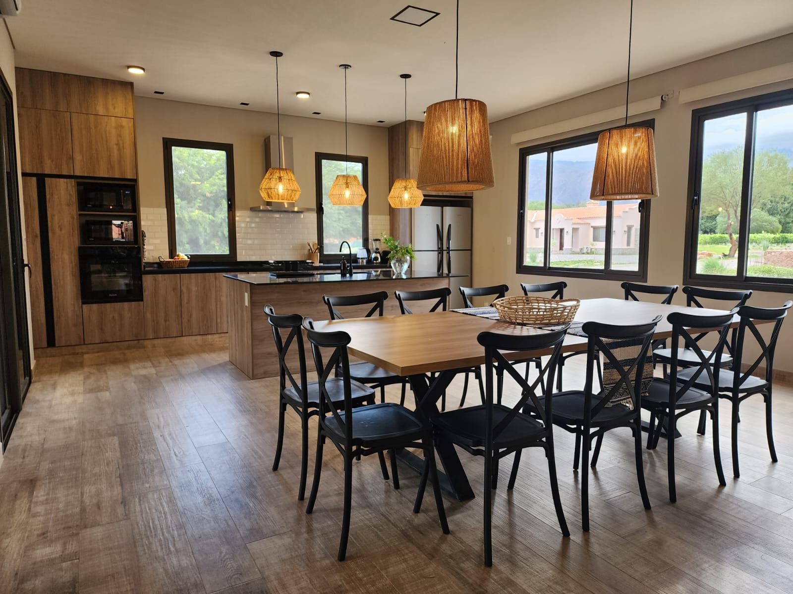 Sala de jantar moderna com ilha de cozinha, pendentes de ratã e piso de madeira — projeto Ca La Estancia, por Luciana González Anderson, em Cafayate