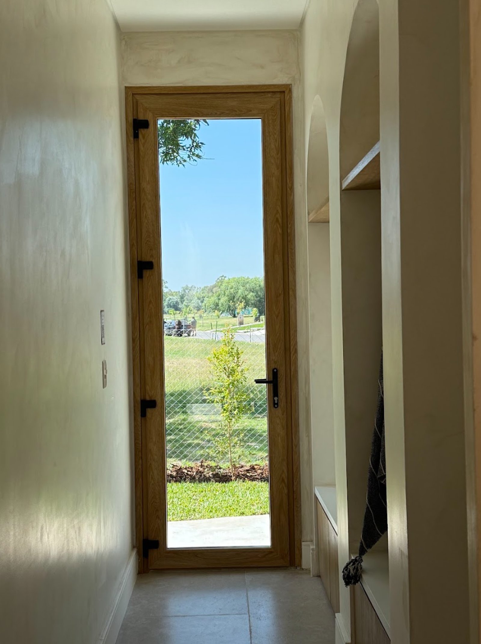Pasillo con puerta de madera y vidrio, nichos arqueados y paredes de microcemento — proyecto La Verbena, por Grupo Pauta Arquitectura, en Alejandro Korn 3150
