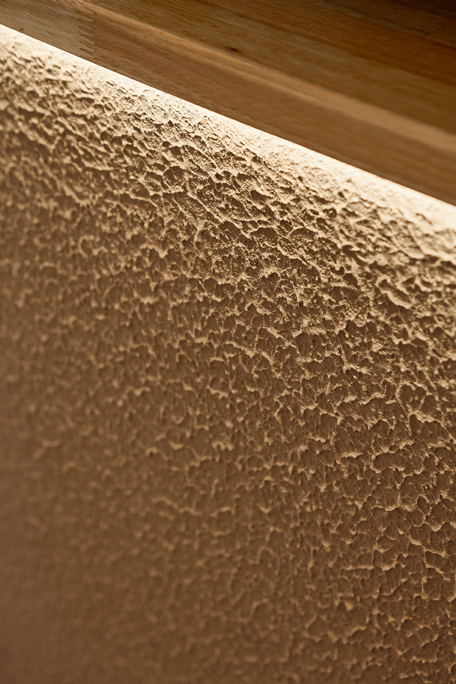 pared de textura rugosa con luz indirecta y detalle de madera — proyecto Severina, por Estudio Plats, en Acoyte 1396
