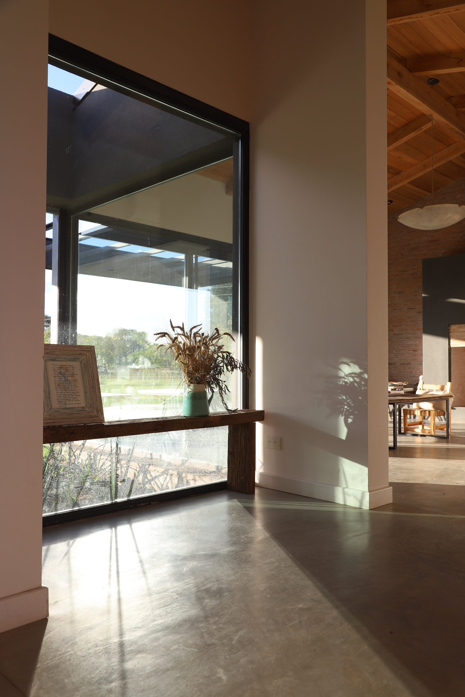 Living moderno con ventanal y vigas de madera — proyecto Casa Areco, por R+B arquitectos, en San Antonio de Areco