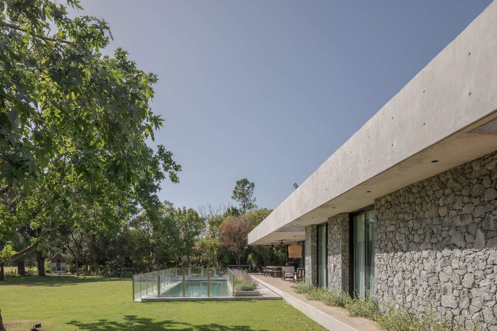 Fachada moderna con muro de piedra, pileta y vegetación — proyecto Casa PLANALTO, por Grupo CRBN, en Av. Pres. Perón 10298