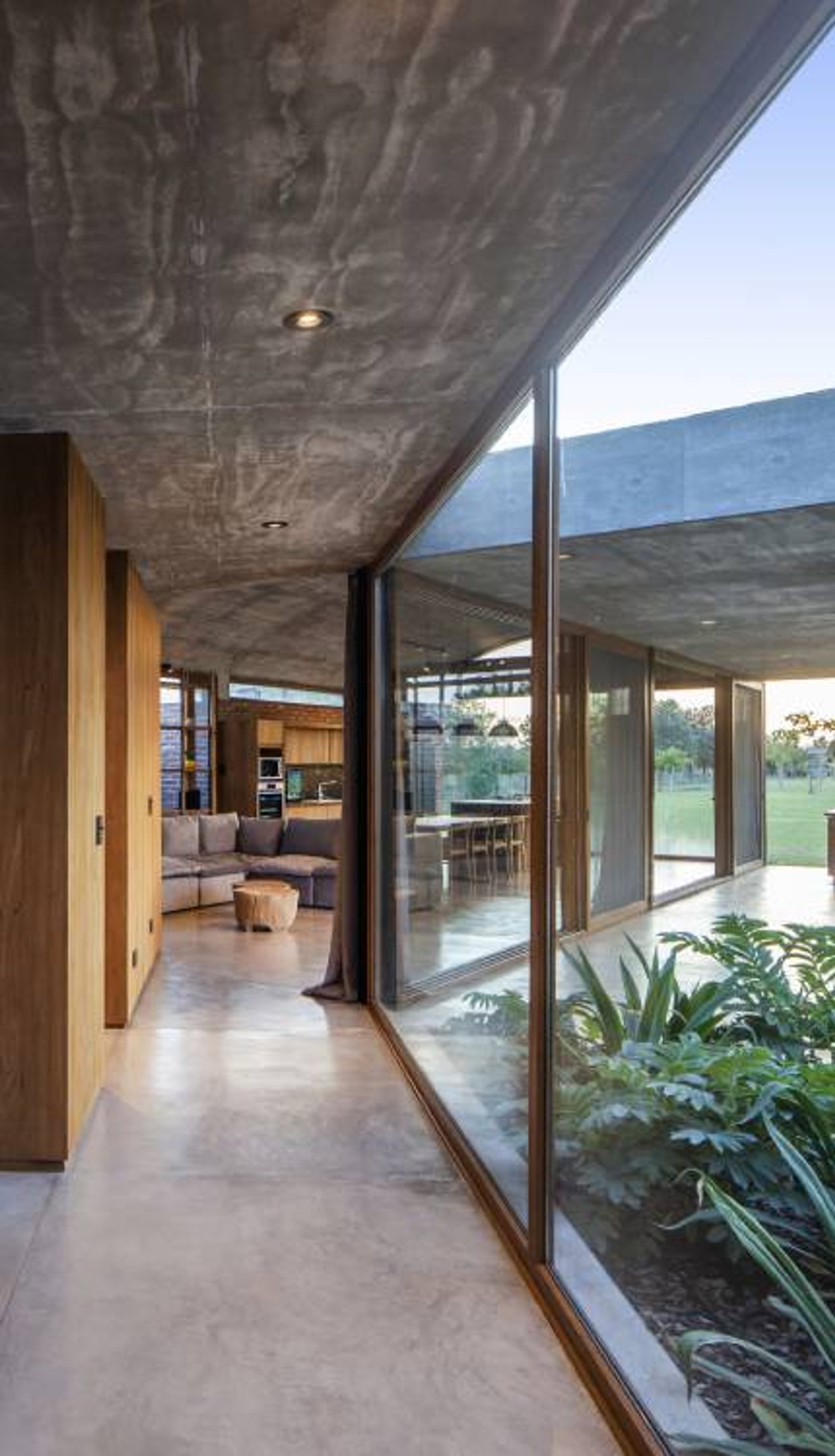 Pasillo moderno con techo de hormigón visto y ventanales al jardín — proyecto Casa Volt, por Estudio PK, en Capilla del Señor