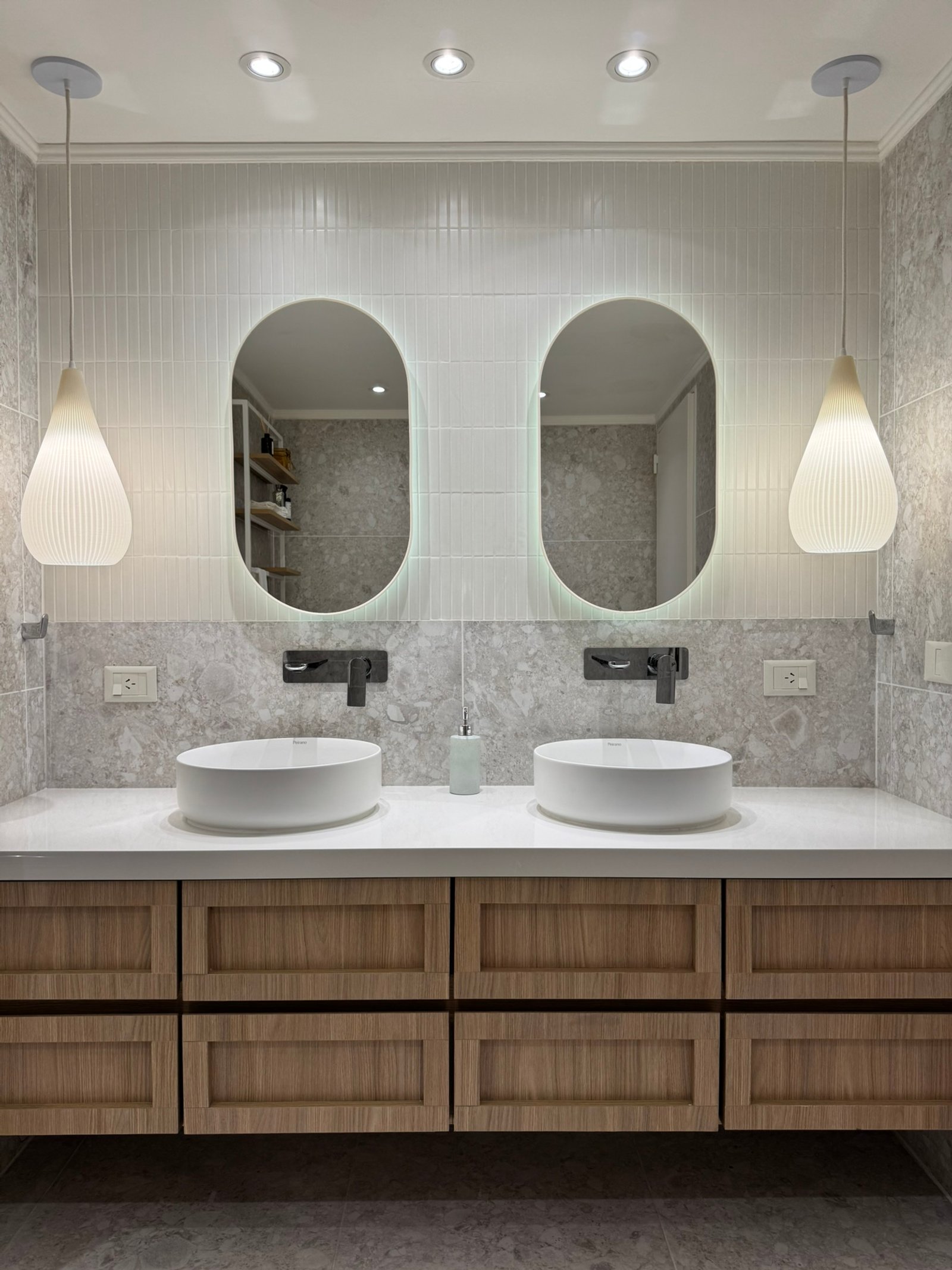 Baño moderno con doble bacha, espejos ovalados retroiluminados y muebles de madera — proyecto Lafinur, por MDBK Arquitectura, en Palermo