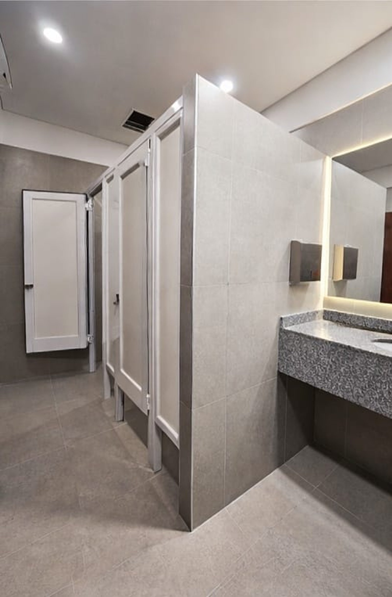 baño comercial moderno con cubículos blancos y detalles grises — proyecto La Virginia , por uniKKo Estudio de Diseño, en Mar del Plata