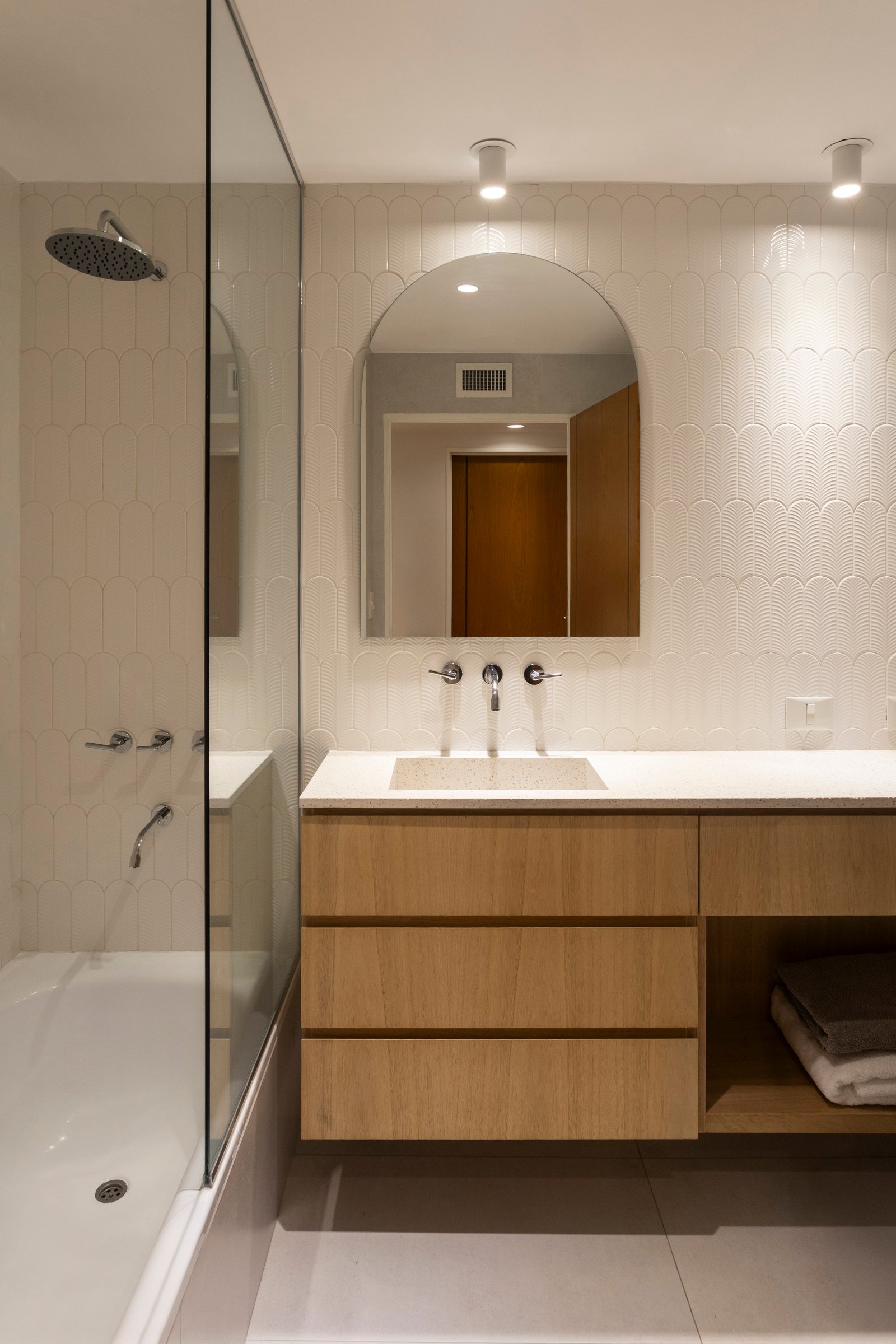 Banheiro moderno com bancada flutuante, espelho arqueado e azulejo curvo — projeto BARRACAS, por La Nave Arq., em Barracas