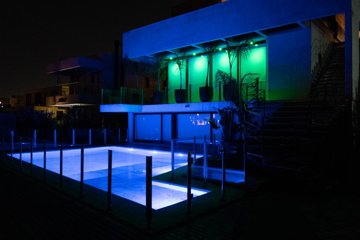 Área de piscina residencial moderna iluminada com luzes azuis à noite — projeto Casa Pomelo, por FeelX Tecnología SRL, em Canning