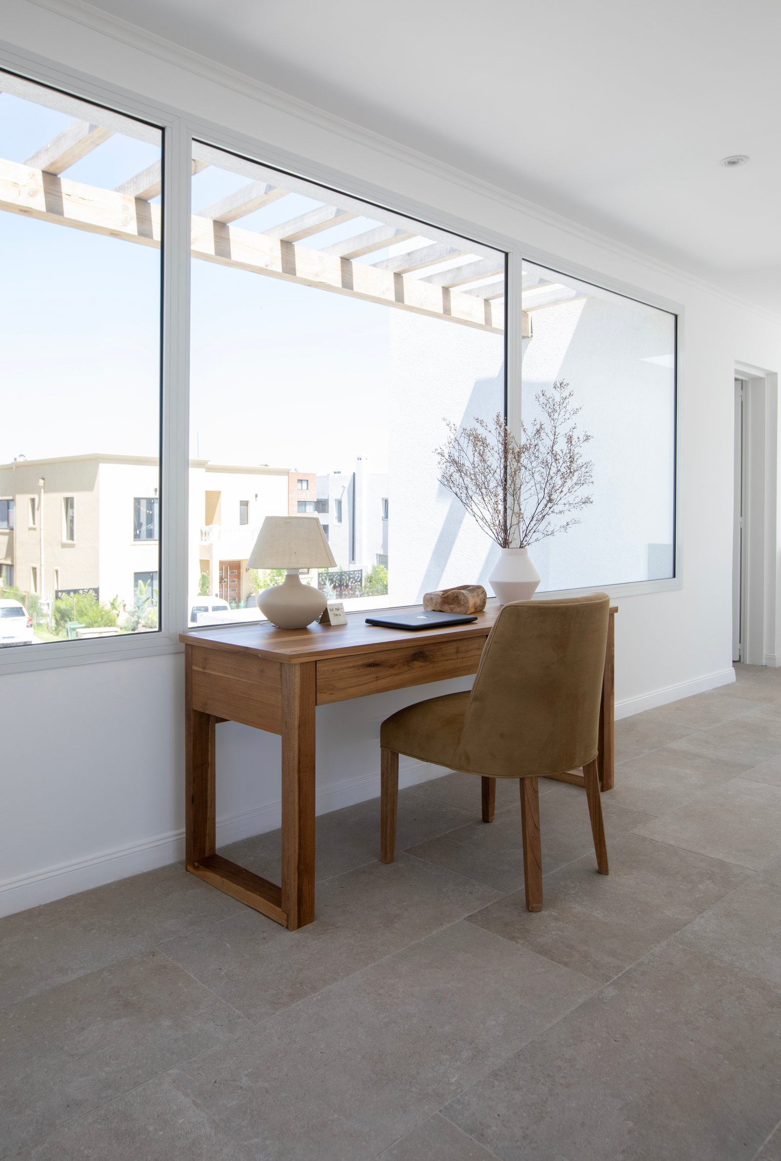 Oficina moderna con escritorio de madera y silla de terciopelo junto a grandes ventanales — proyecto OBRA LE PIETRE DEL CASALE SABBIA, por ILVA, en Provincia de Buenos Aires
