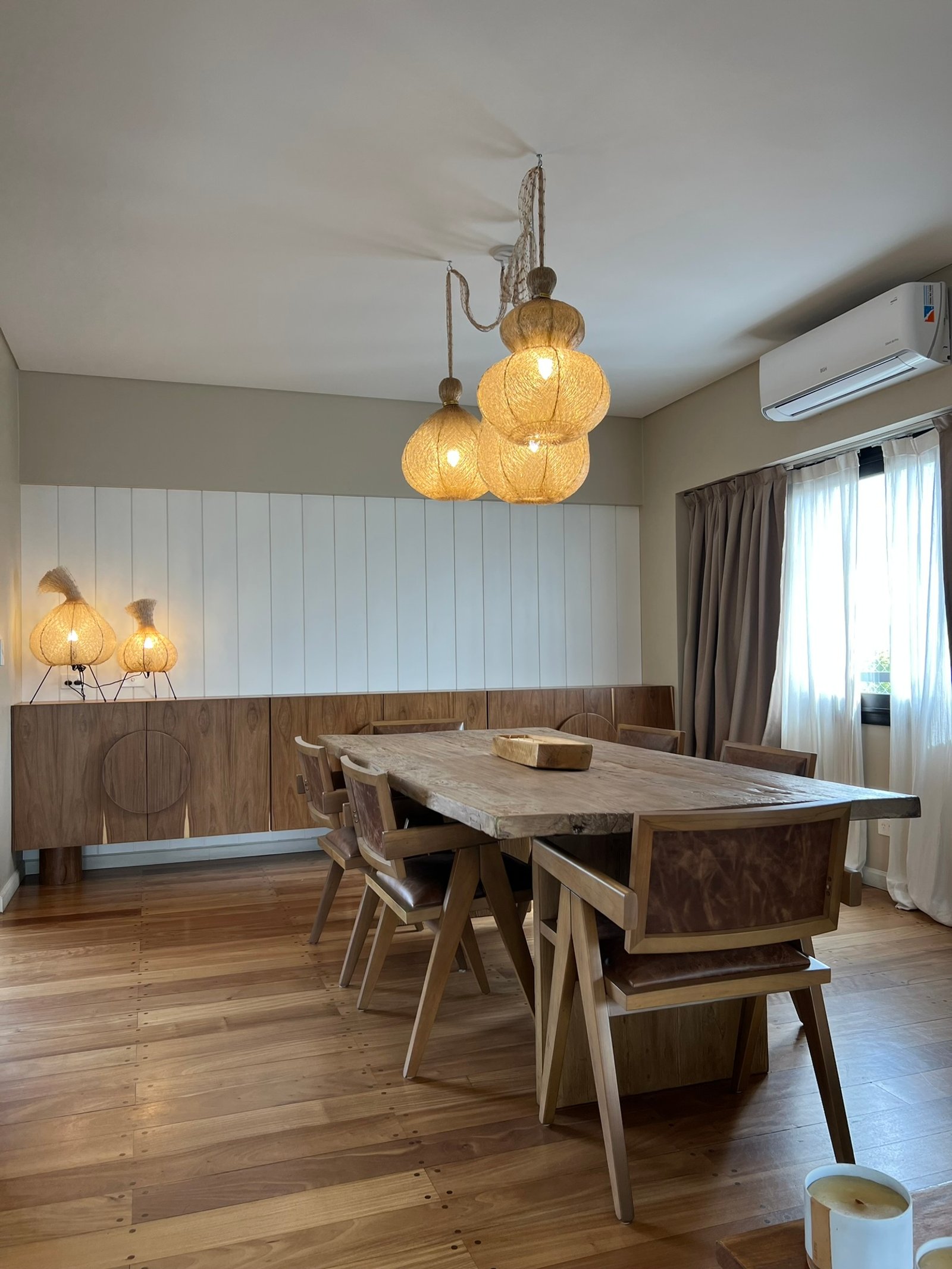 Sala de jantar rústica com mesa de madeira e lustres de rattan — projeto Vallejos, por MDBK Arquitectura, em Villa Devoto