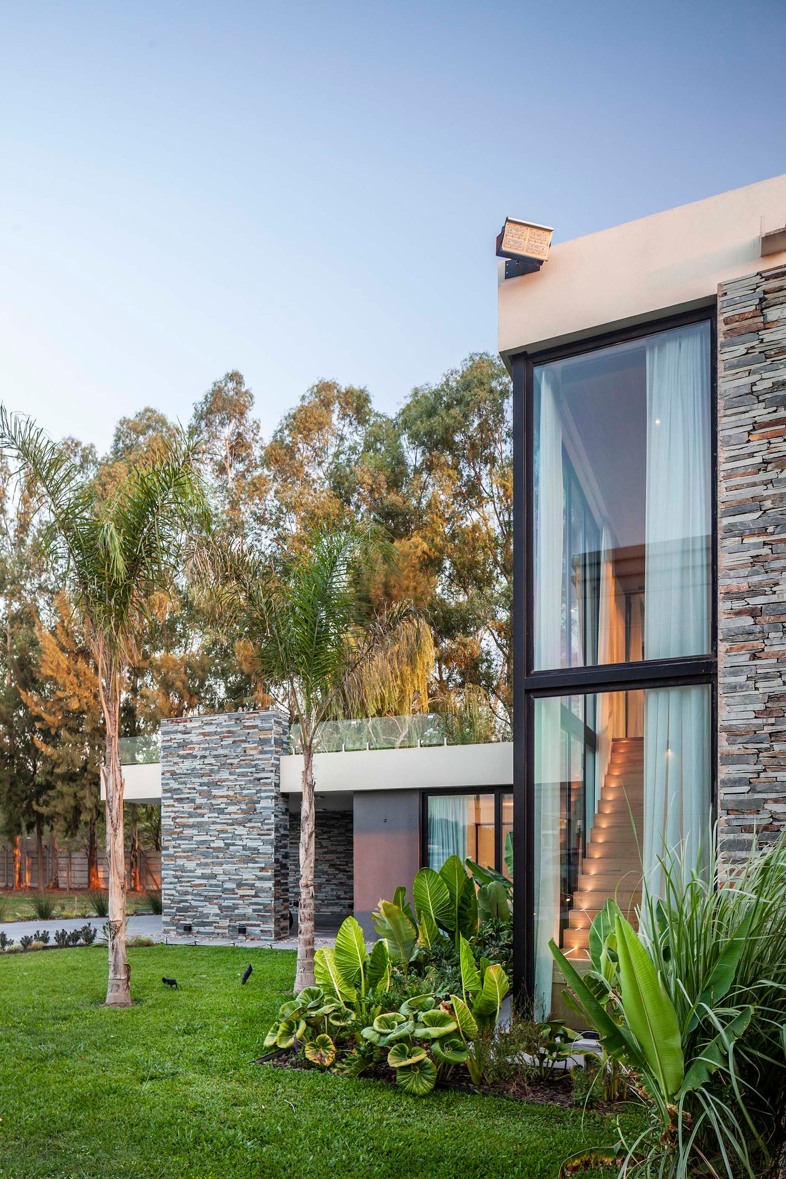 fachada moderna con ventanales y jardin tropical — proyecto CASA T199, por A'PRIMA - Arquitectura Sustentable, en Los Robles 5901