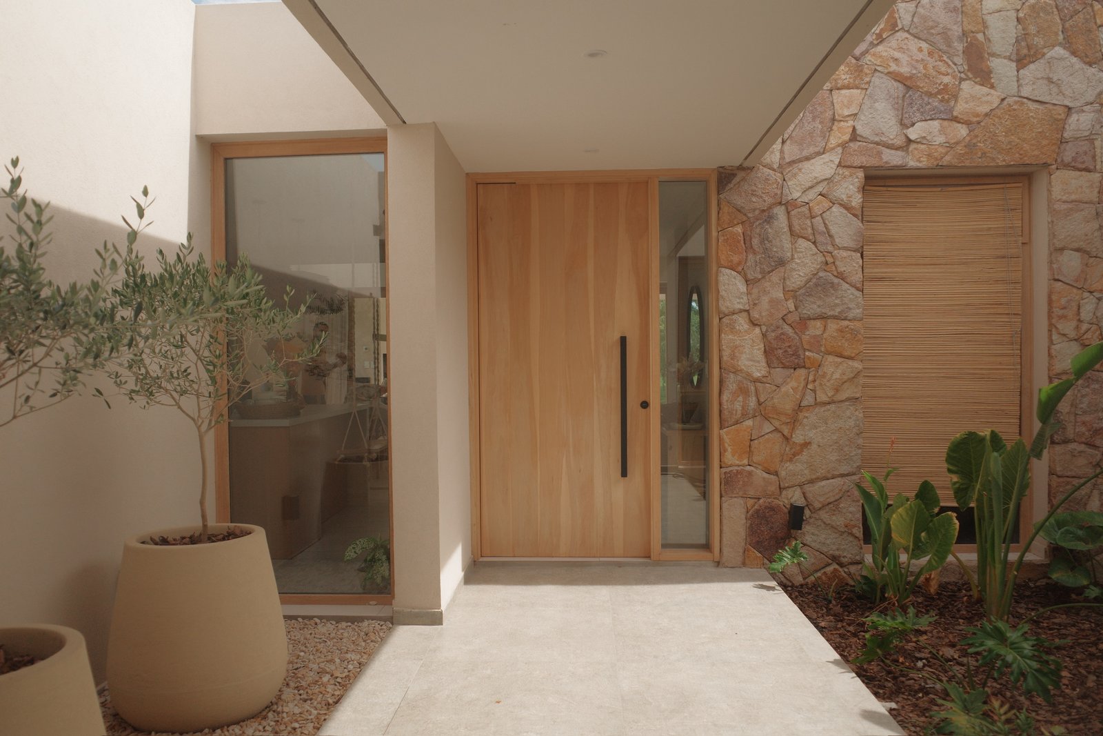 Entrada moderna con muro de piedra y madera, puerta principal de madera y maceta grande — proyecto Casa Refugio, por Jeitinho Estudió Creativo, en Neuquén