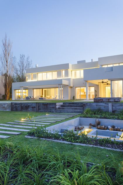 Fachada moderna con jardín escalonado al atardecer — proyecto Modernismo Náutico, por Apaarquitectura, en Tigre
