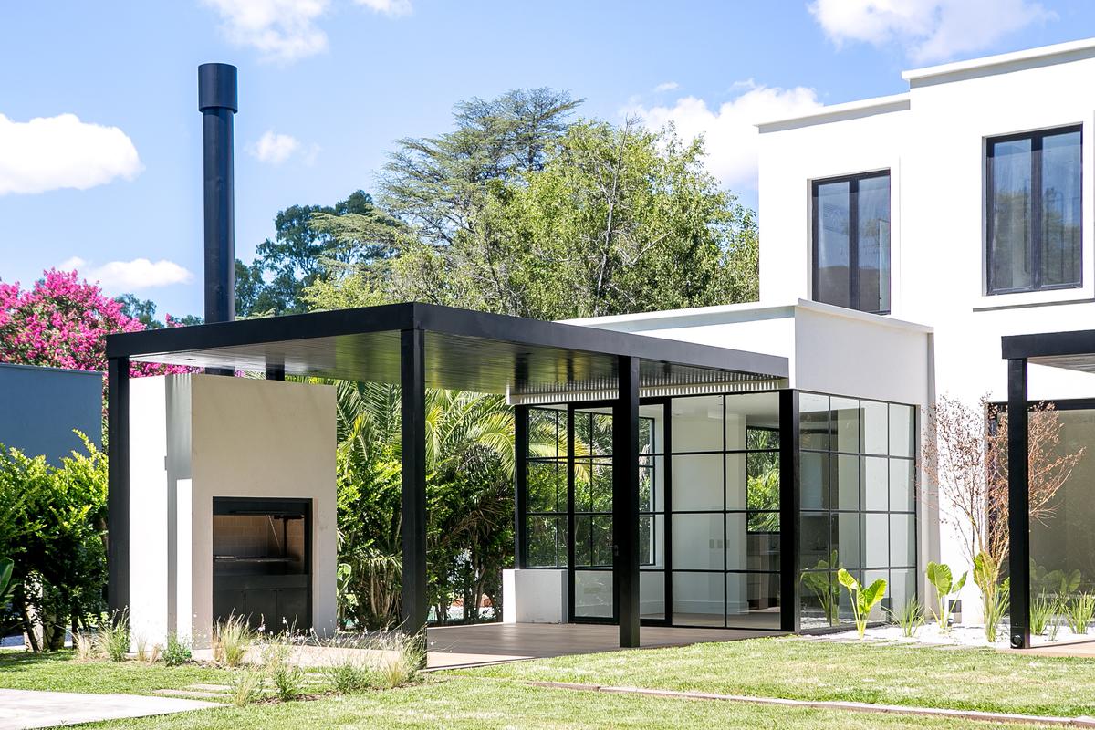 Fachada moderna com pérgula de metal preto e janelas de vidro no jardim — projeto Bosque Chico, por Estudio Arq. María Sioli, em Garin
