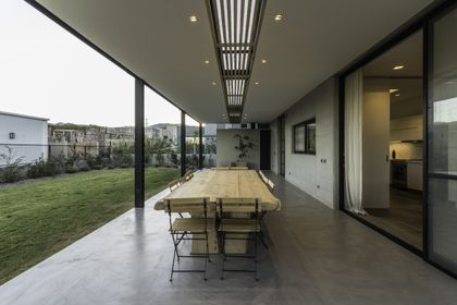 Galería cubierta contemporánea con mesa de madera, ventanales y jardín al fondo — proyecto CASA ARFE, por Valeria Valdivieso Arquitecta, en Ciudad de Mendoza
