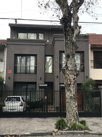 Casa moderna gris con frente de hormigón, grandes ventanales y árbol frondoso — proyecto Devoto, por Rioja Arquitectura, en CABA