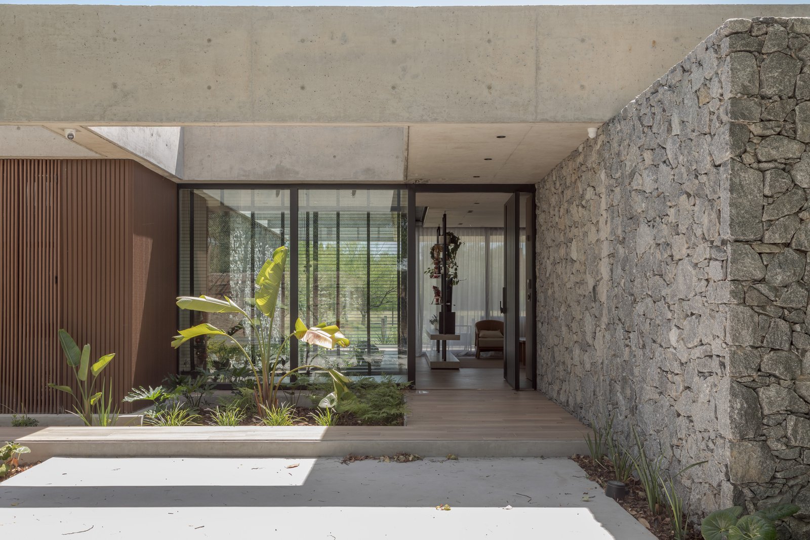Fachada moderna com pedra, madeira e pátio interno visível — projeto Casa PLANALTO, por Grupo CRBN, em Av. Pres. Perón 10298