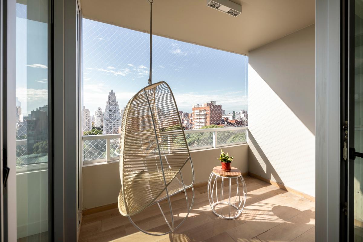 Varanda moderna com cadeira de vime suspensa e vista urbana — projeto Mirabilia, por Estudio Basa, em Buenos Aires