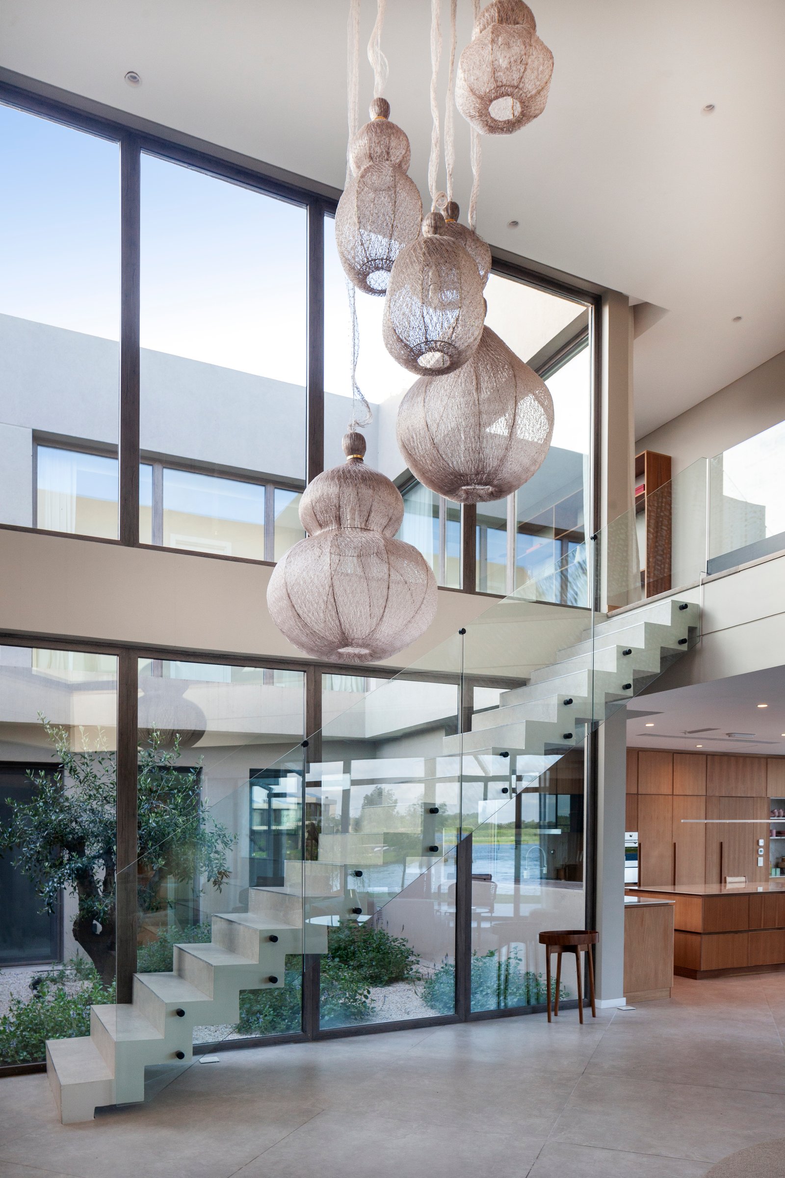 Amplio interior moderno con escalera flotante y lámparas colgantes de ratán — proyecto CASA M40, por A'PRIMA - Arquitectura Sustentable, en Unnamed Road