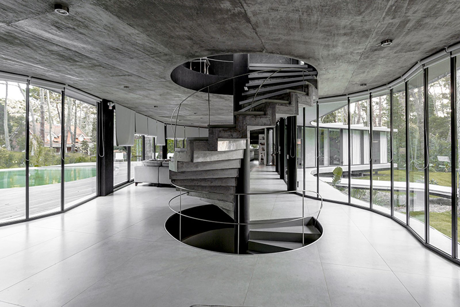 Interior moderno com escada em espiral de concreto e janelas do chão ao teto — projeto Casa Ameba, por MUCHTEK, em B7167 Cariló