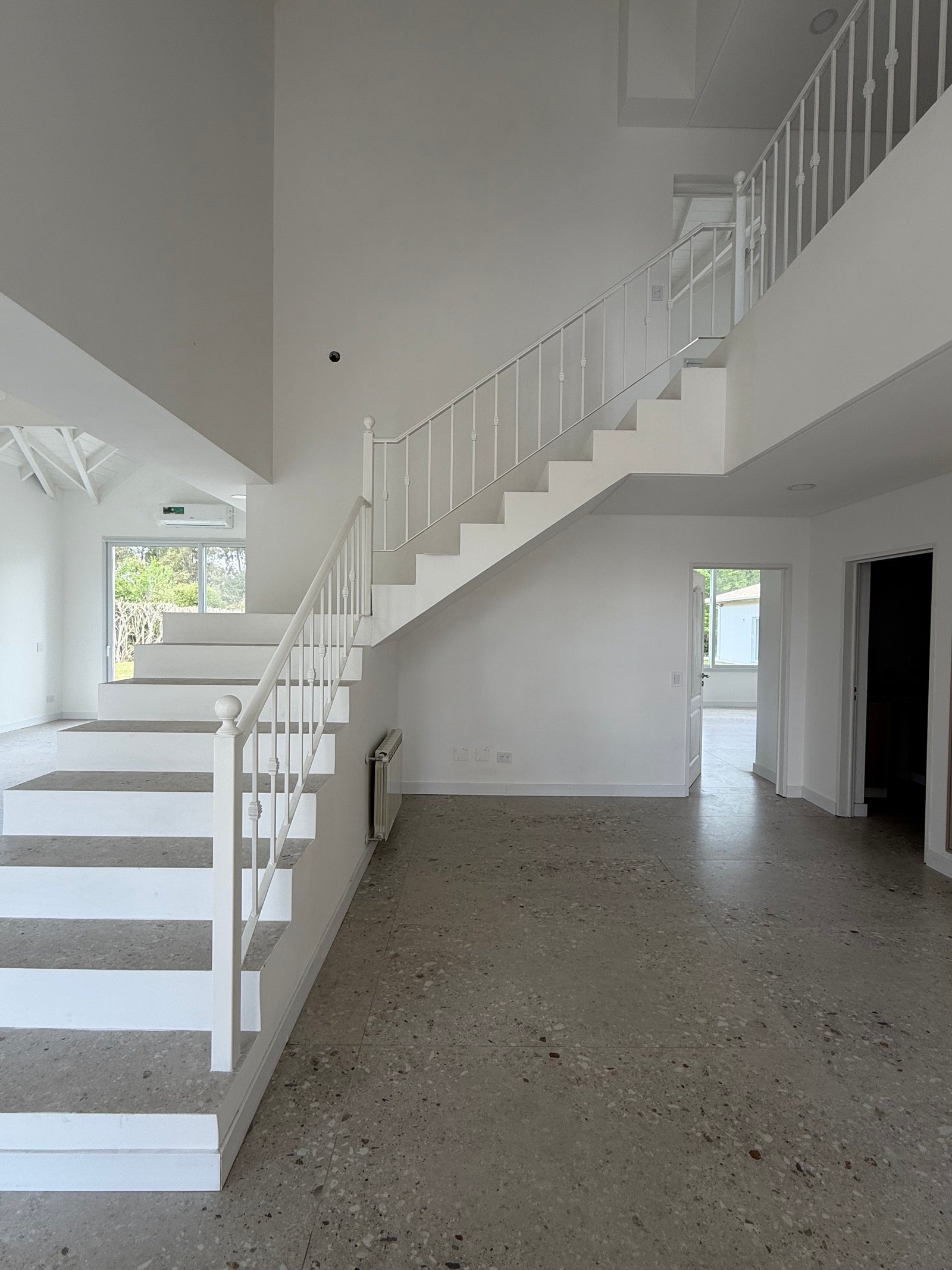 Interior moderno de doble altura con escalera flotante y piso de terrazo — proyecto CASA LA CASUALIDAD , por Estudio Grupo 32, en Pilar