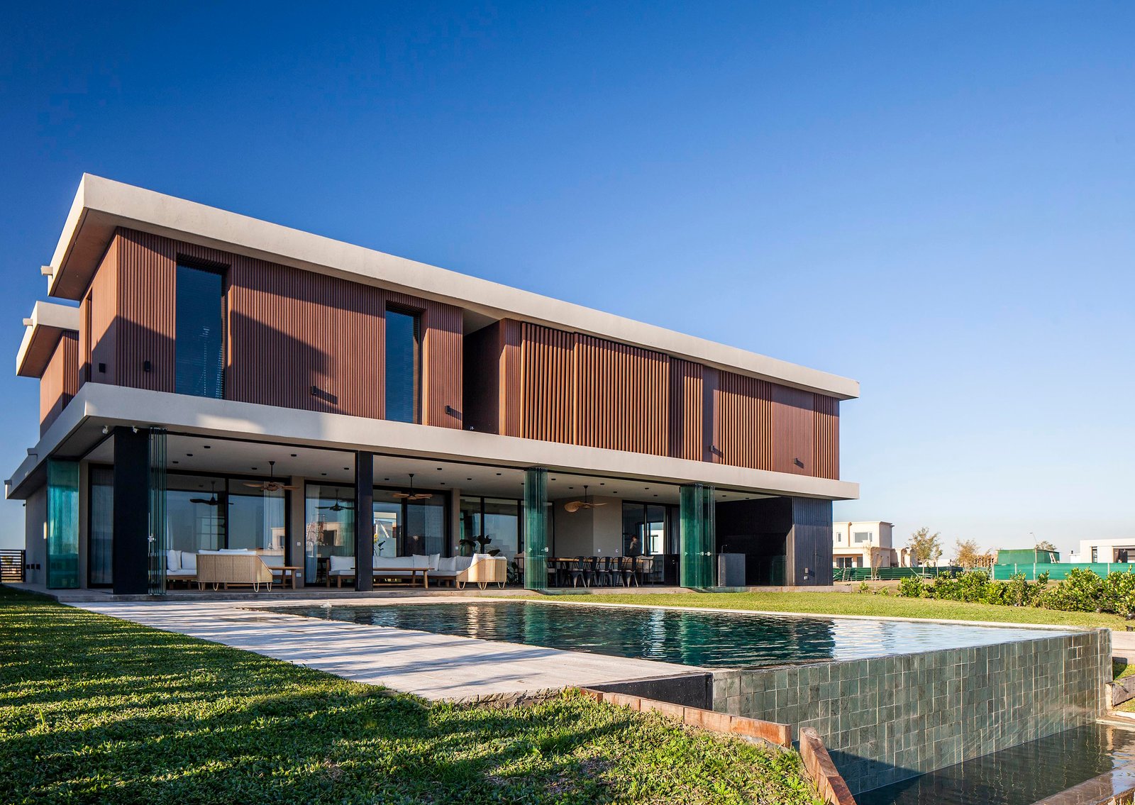 fachada moderna de madera y concreto con piscina — proyecto CASA C313, por A'PRIMA - Arquitectura Sustentable, en Provincia de Buenos Aires