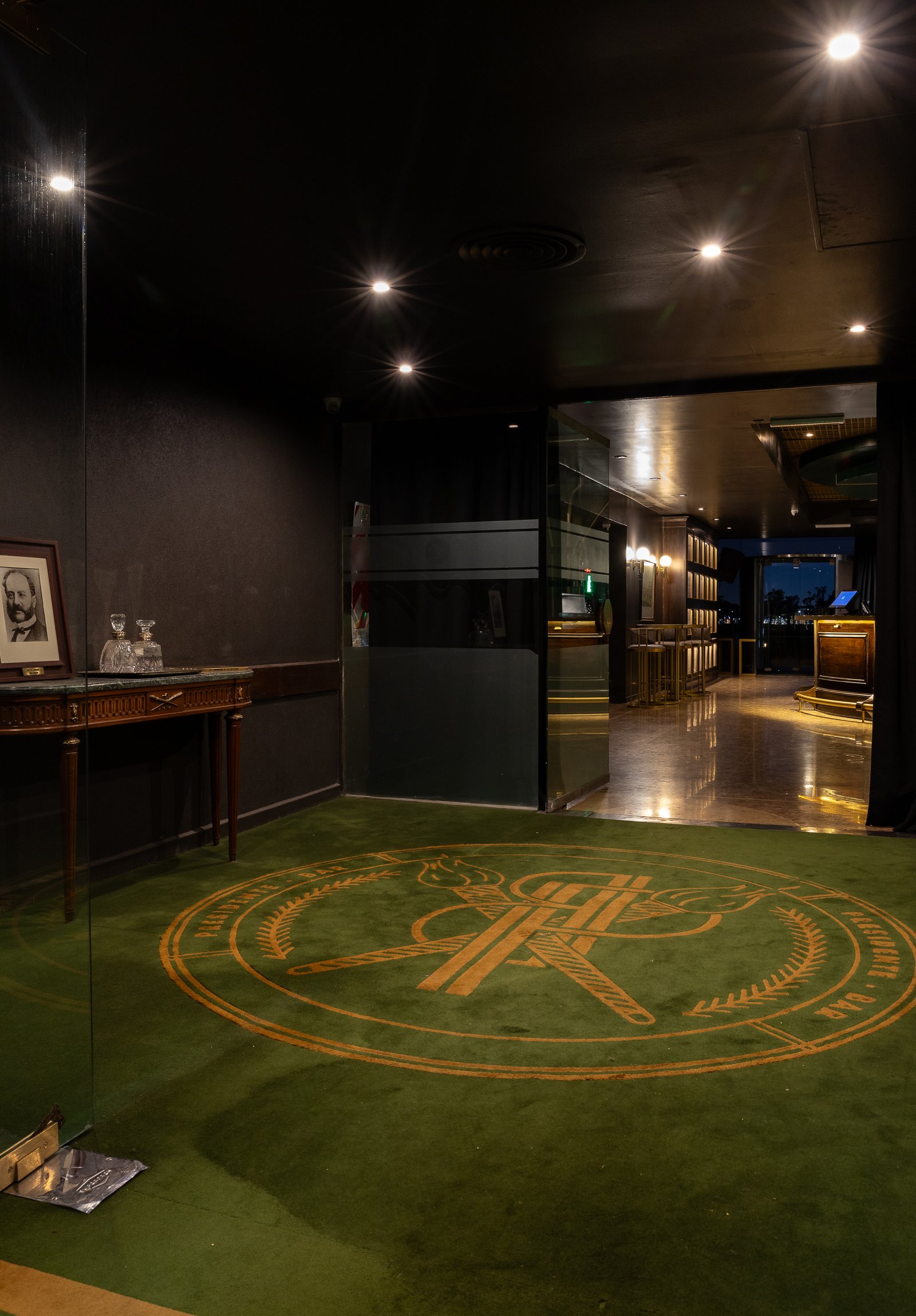 Alfombra circular con logo, iluminación cálida y detalles en madera — proyecto PRESIDENTE BAR HIPODROMO, por AB ARQUITECTURA, en San Isidro