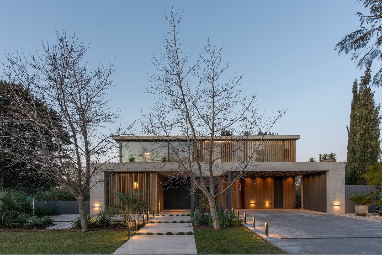 Fachada de casa moderna con madera y concreto, iluminación cálida — proyecto obra Maui, por lifecycle, en Bancalari