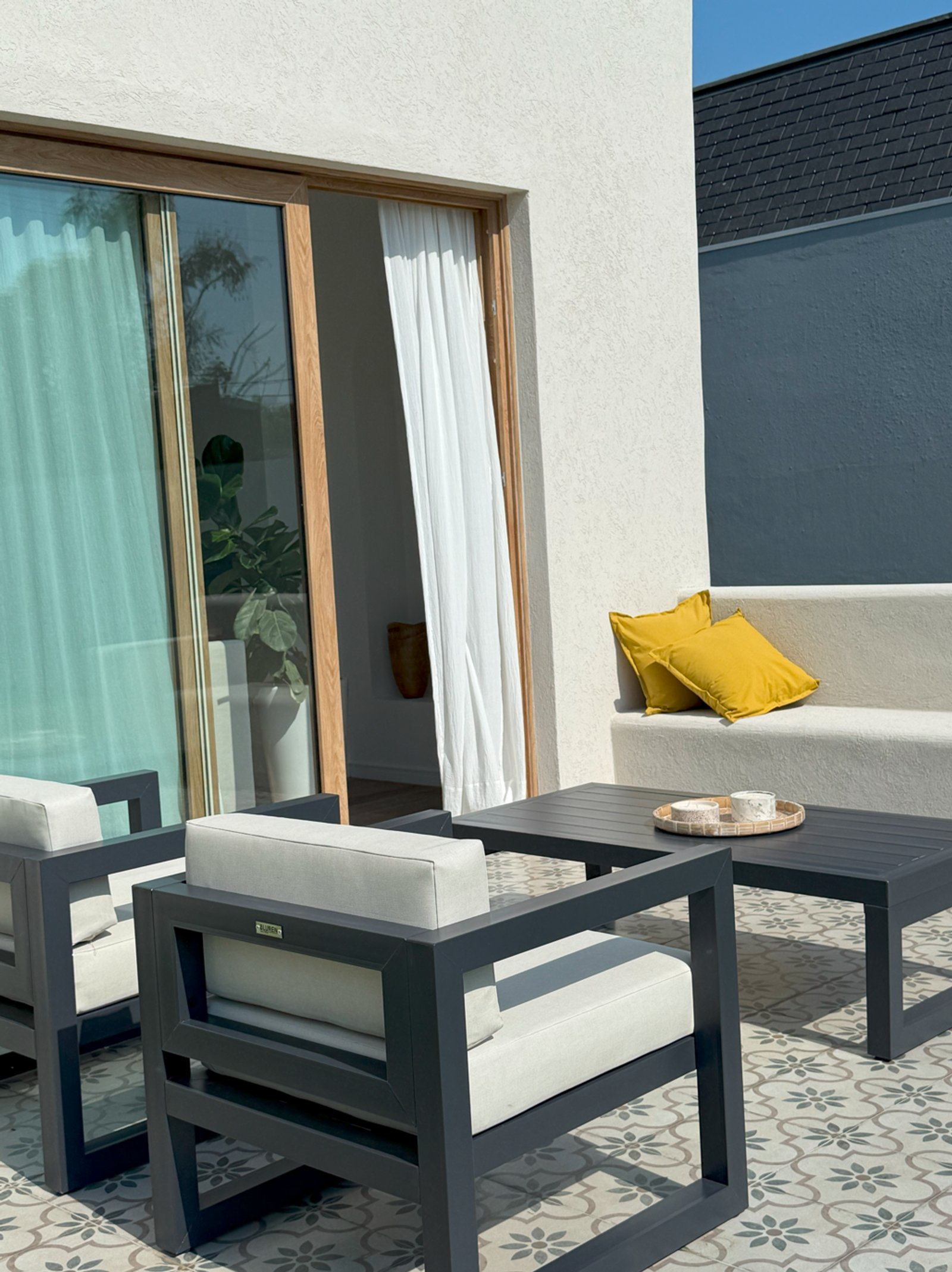 Patio moderno con muebles grises, puertas de vidrio y cortinas blancas — proyecto Exteriores, por CASA1-TROMEN, en Bella Vista