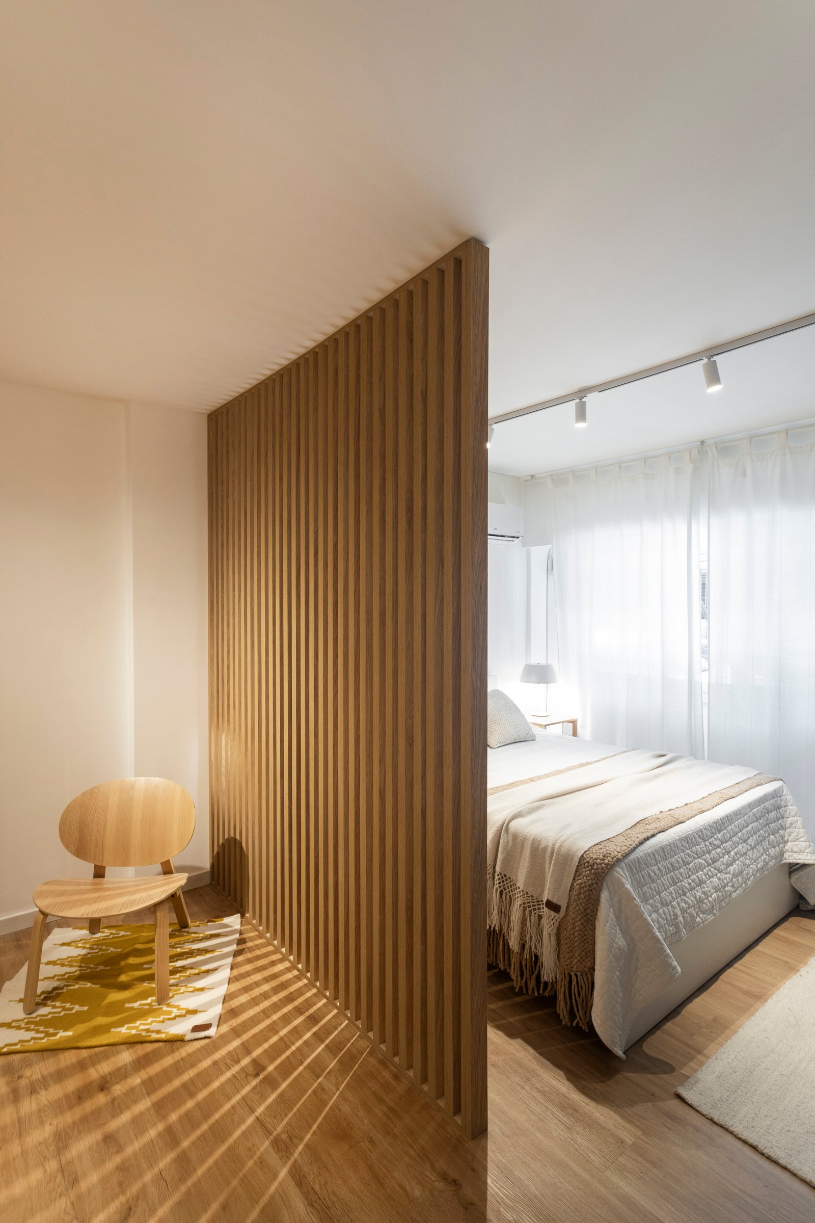 Dormitorio con divisor de listones de madera y silla minimalista — proyecto REFORMA NE, por Rastro Estudio, en Palermo